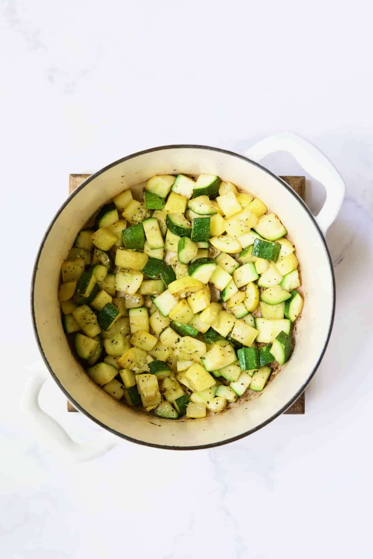 Process photo of zucchini and yellow squash being cooked in white Dutch oven.
