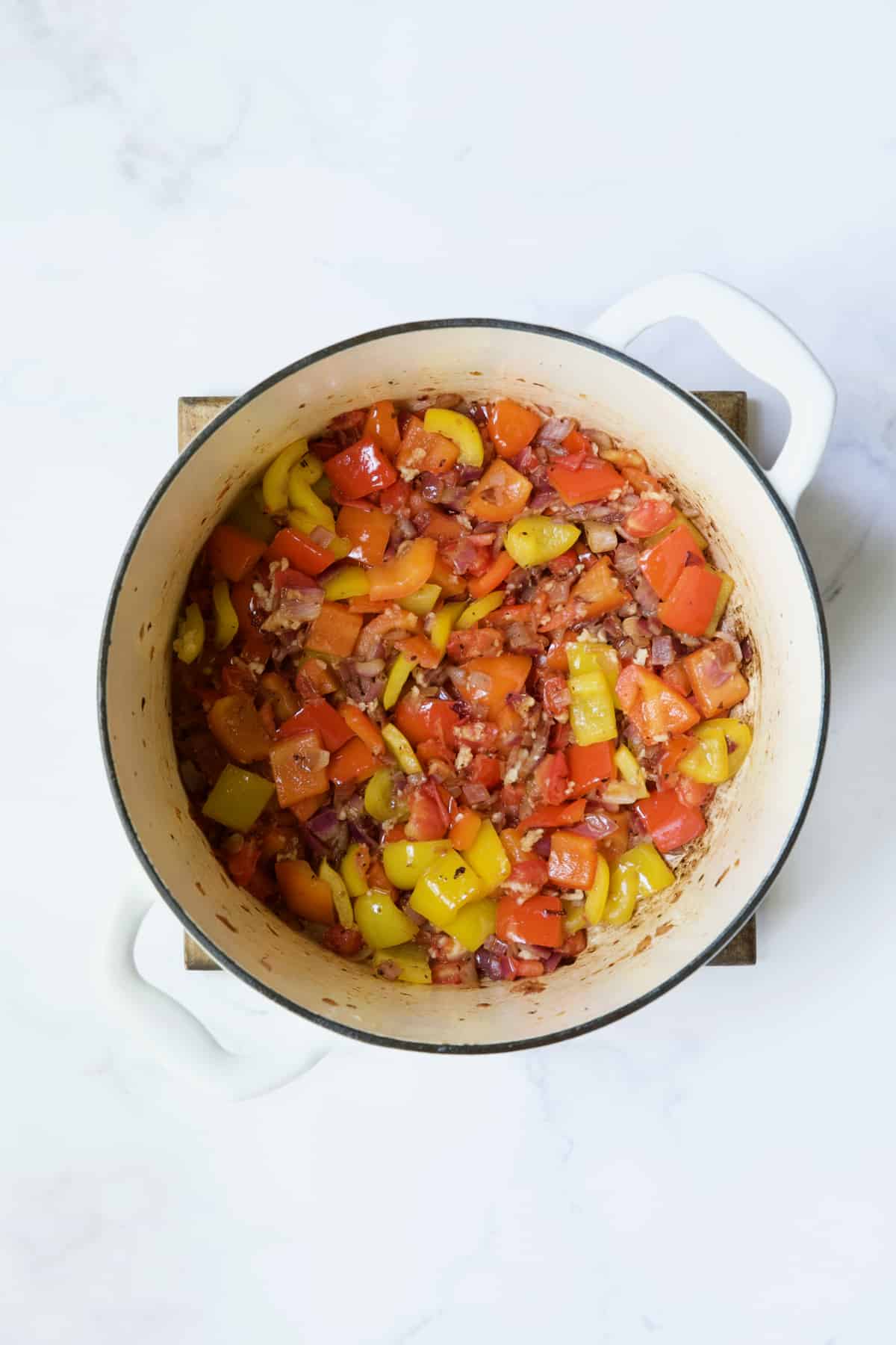 Process photo of onions and peppers being cooked in white Dutch oven.