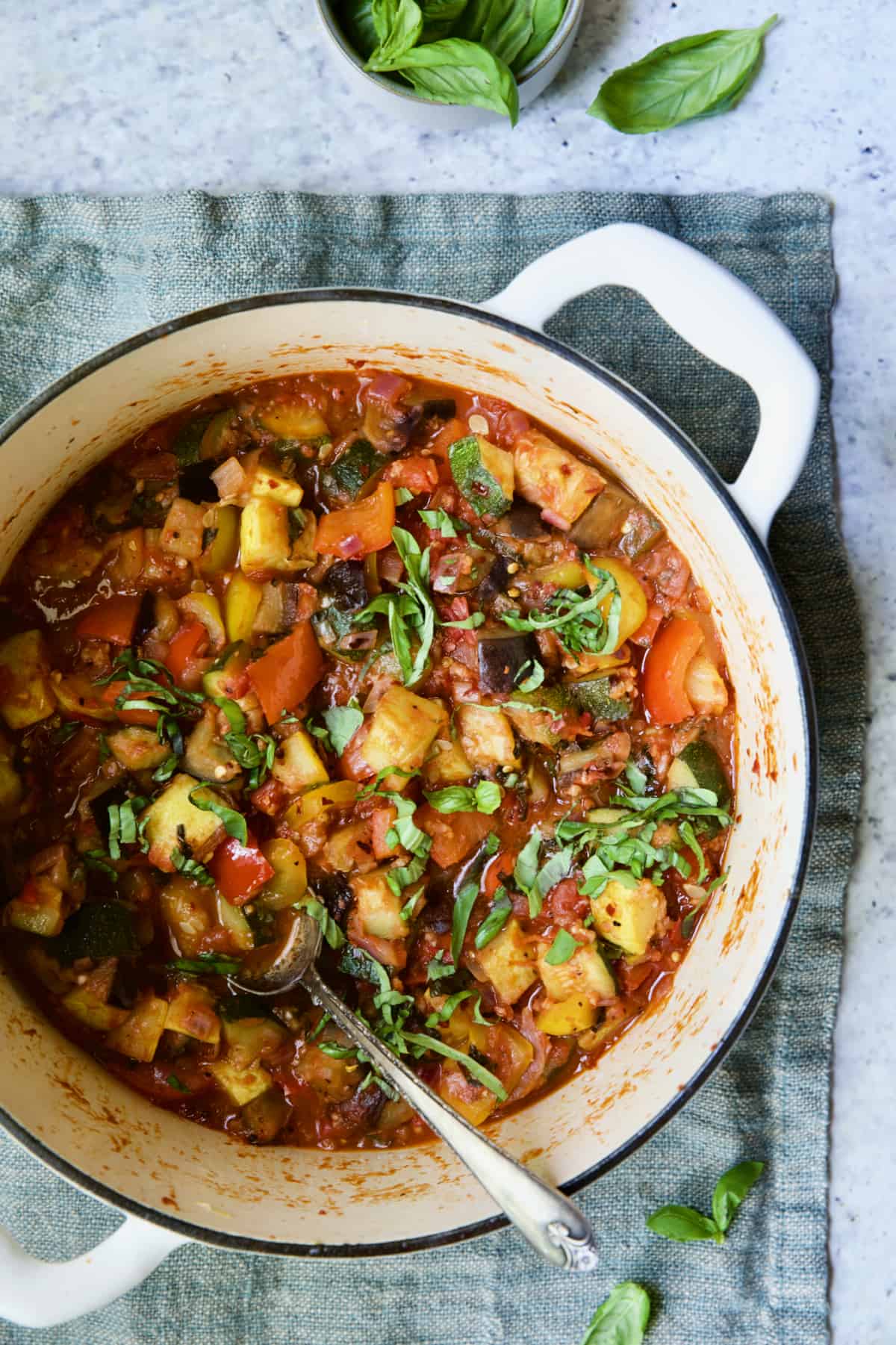 Classic French Ratatouille in white Dutch oven garnished with fresh basil.