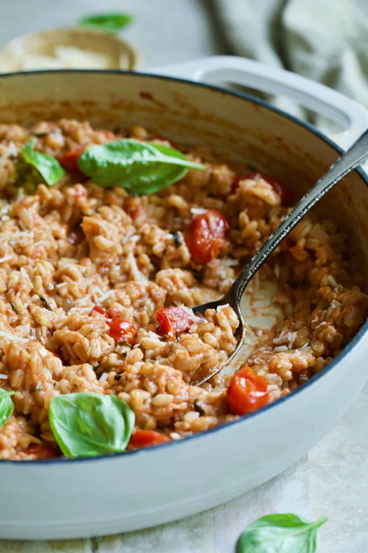 Tomato Farro Risotto with Basil and Parmesan in white cast iron skillet with serving spoon.