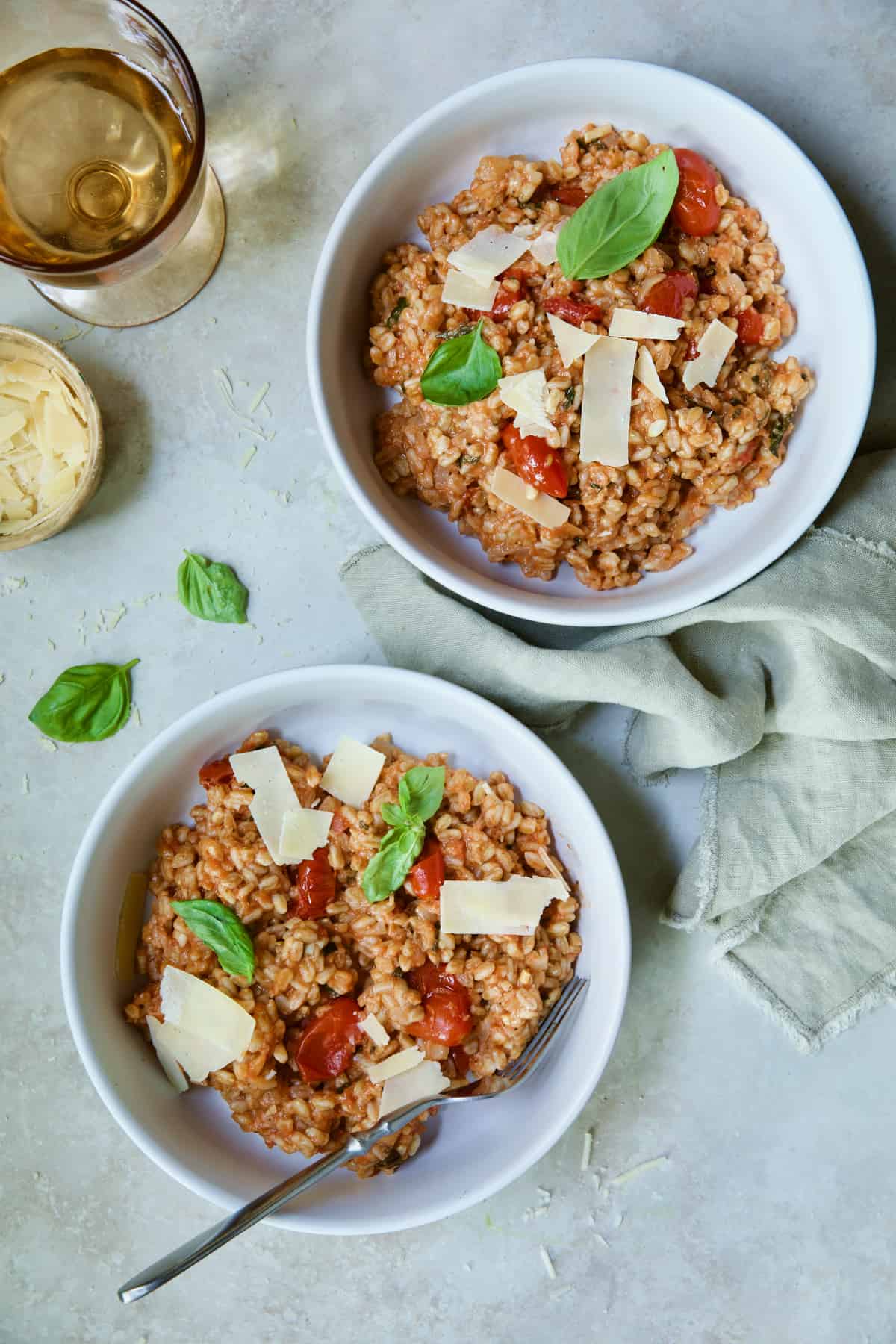 Two servings of Tomato Farro Risotto with Basil and Parmesan in white bowls garnished with basil leaves.