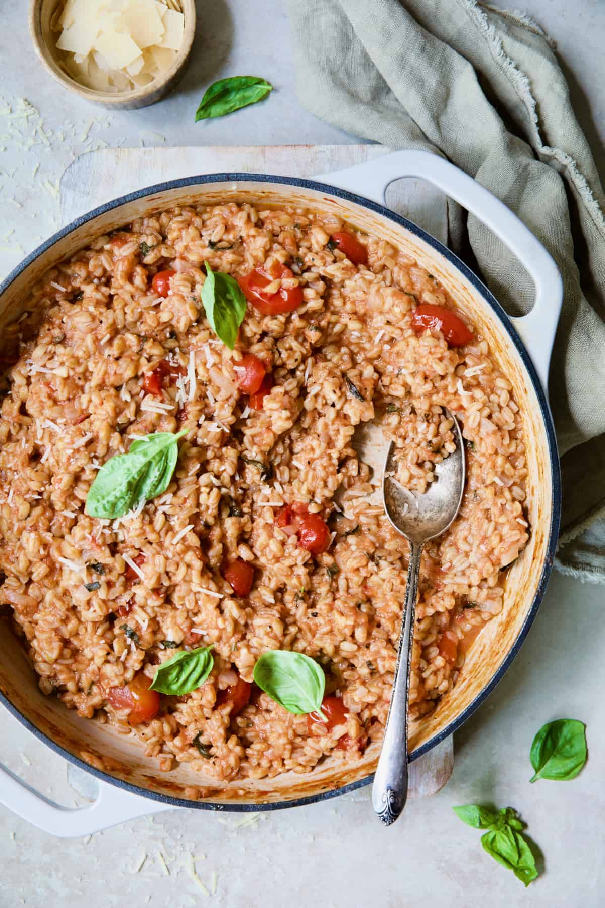 Tomato Farro Risotto with Basil and Parmesan in white enameled cast iron skillet garnished with fresh basil.