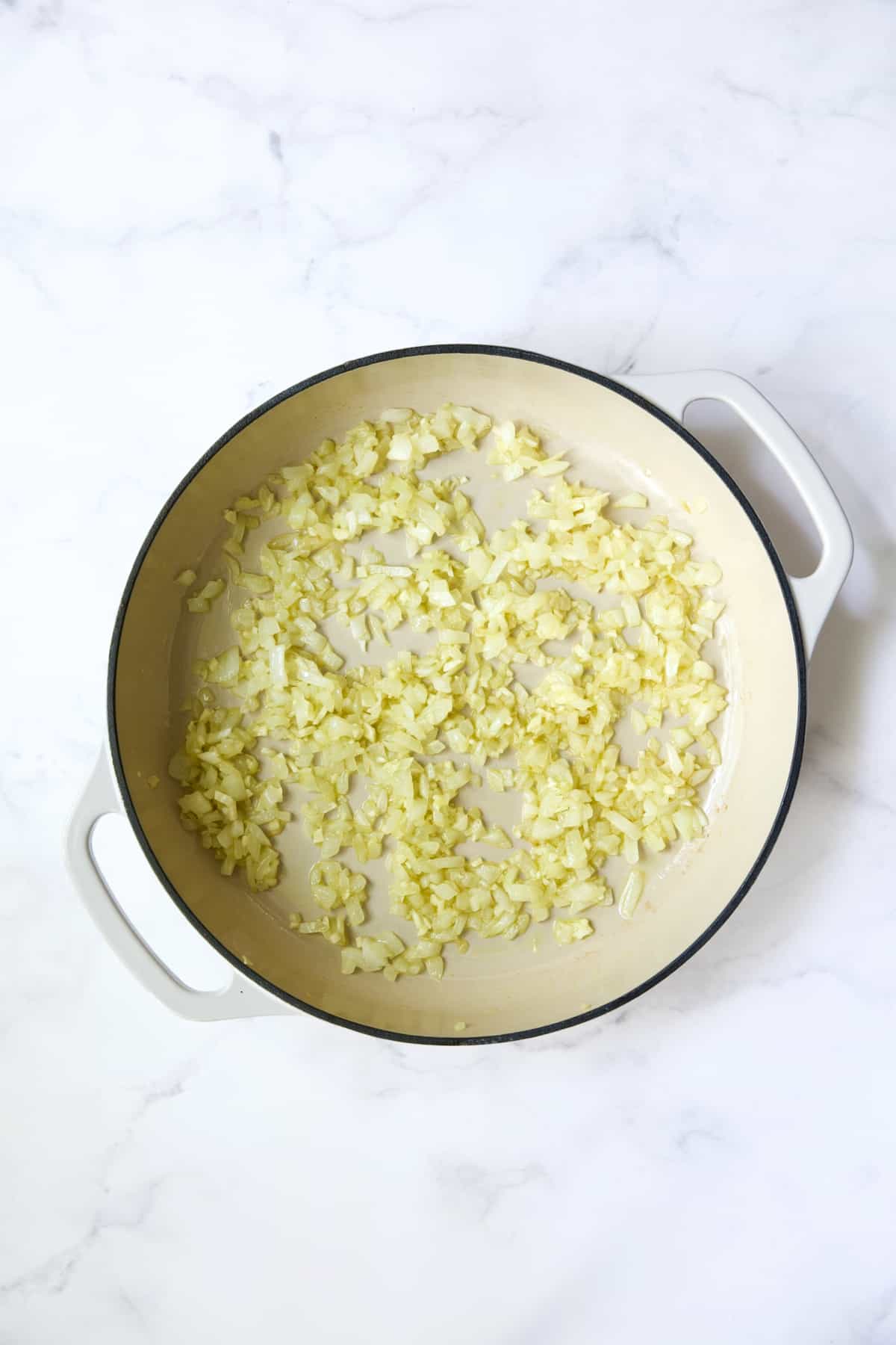 Onions being cooked in white cast iron enamel skillet.