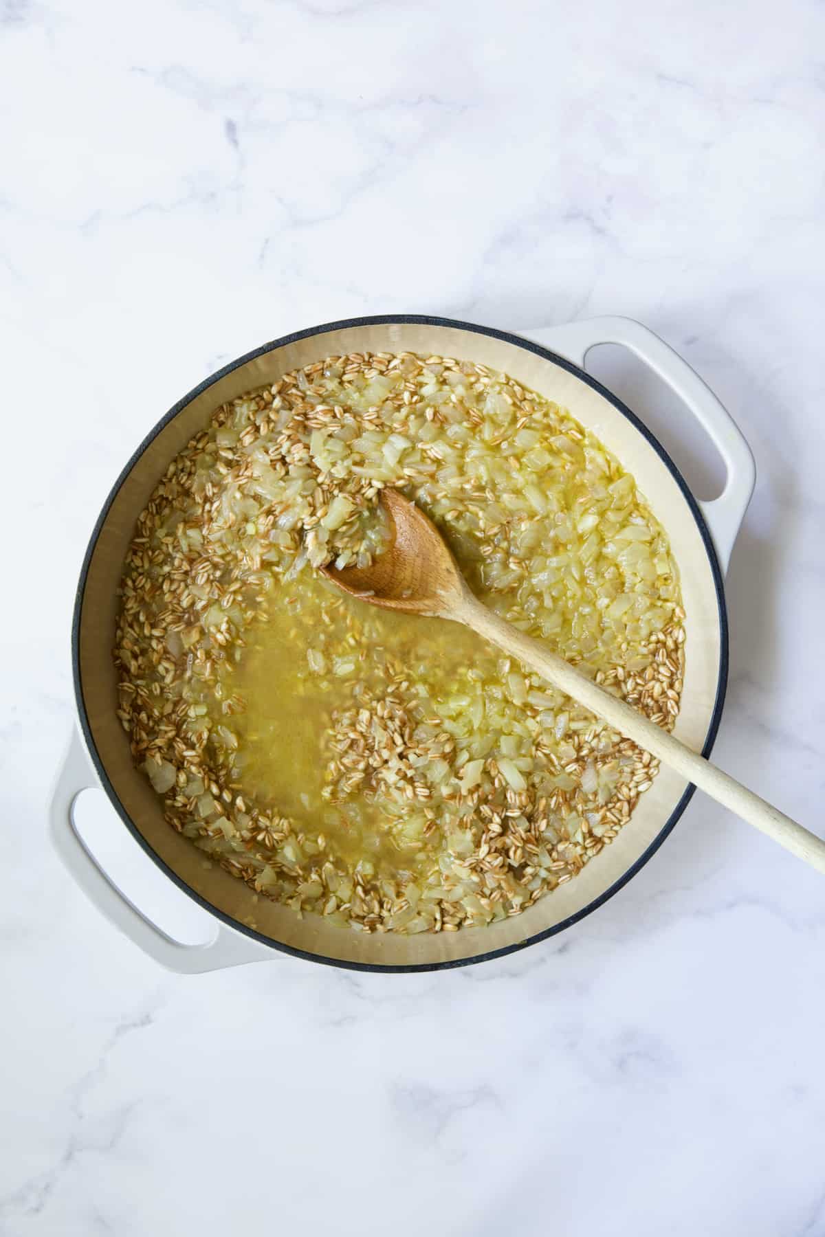 Process photo after broth is added being stirred with wooden spoon.