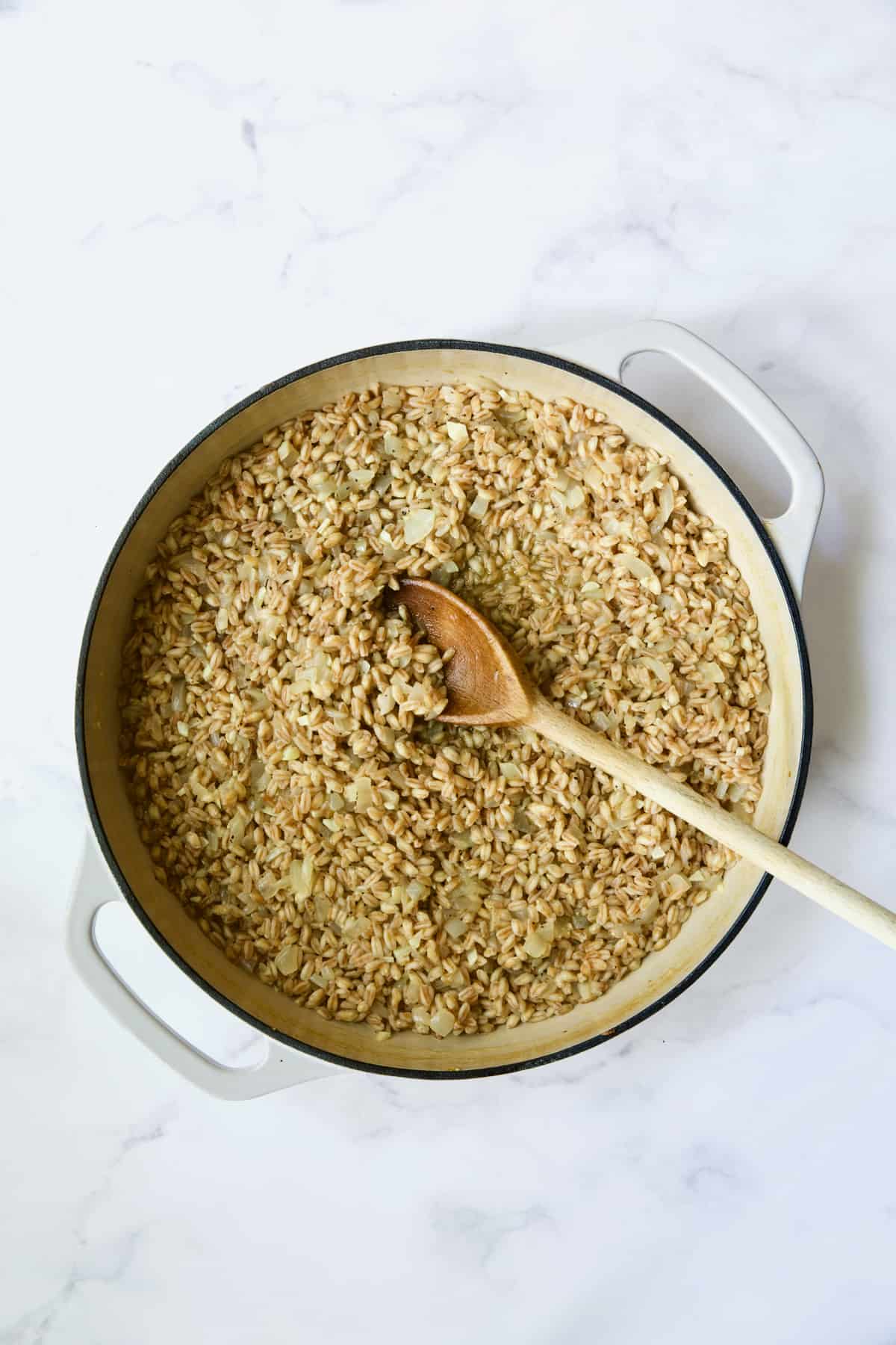 Process photo of farro risotto after broth is absorbed being stirred with wooden spoon.