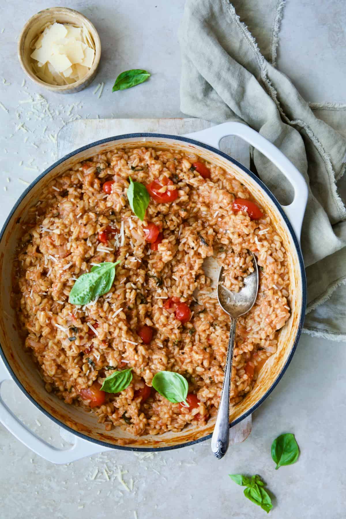 Tomato Farro Risotto with Basil and Parmesan in white cast iron enamel skillet with serving spoon.