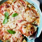 Crustless Southern Tomato Pie in light blue pie pan garnished with fresh basil with a piece cut out and about to be served.