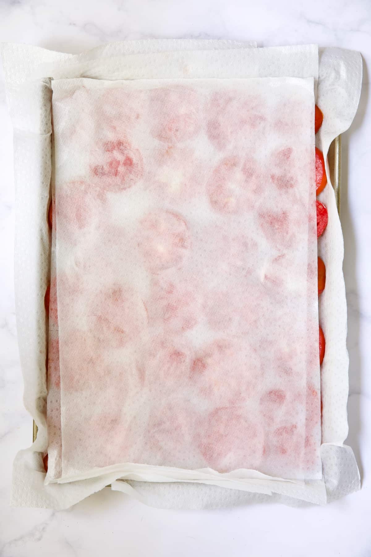 Tomatoes on paper towel-lined baking sheet with paper towels blotting tomatoes dry.