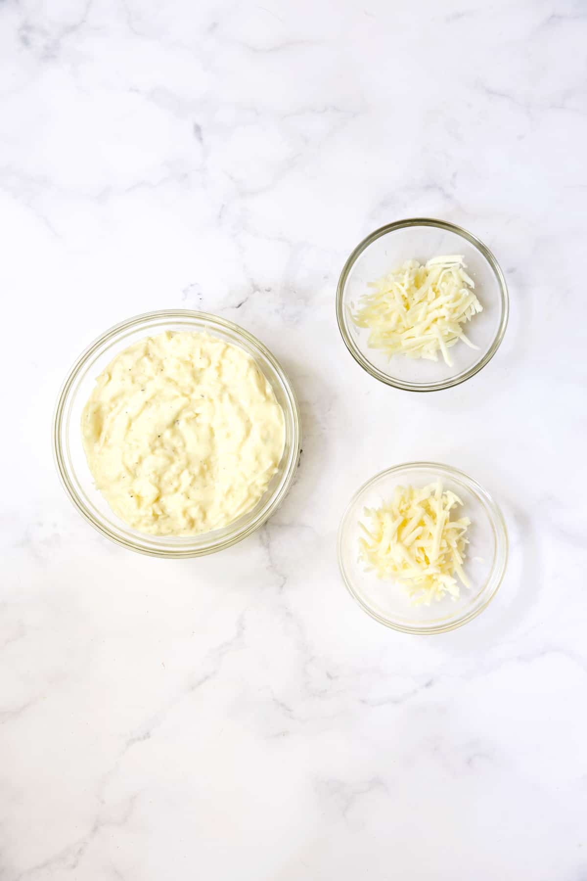 Mayonnaise and cheese mixture in glass bowl with two small bowls of cheese.