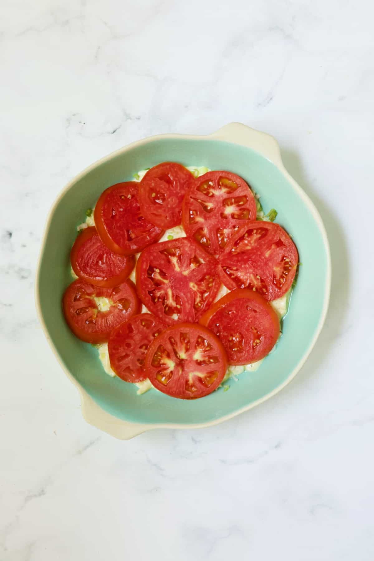 First layer of tomatoes for tomato pie in blue pie pan.