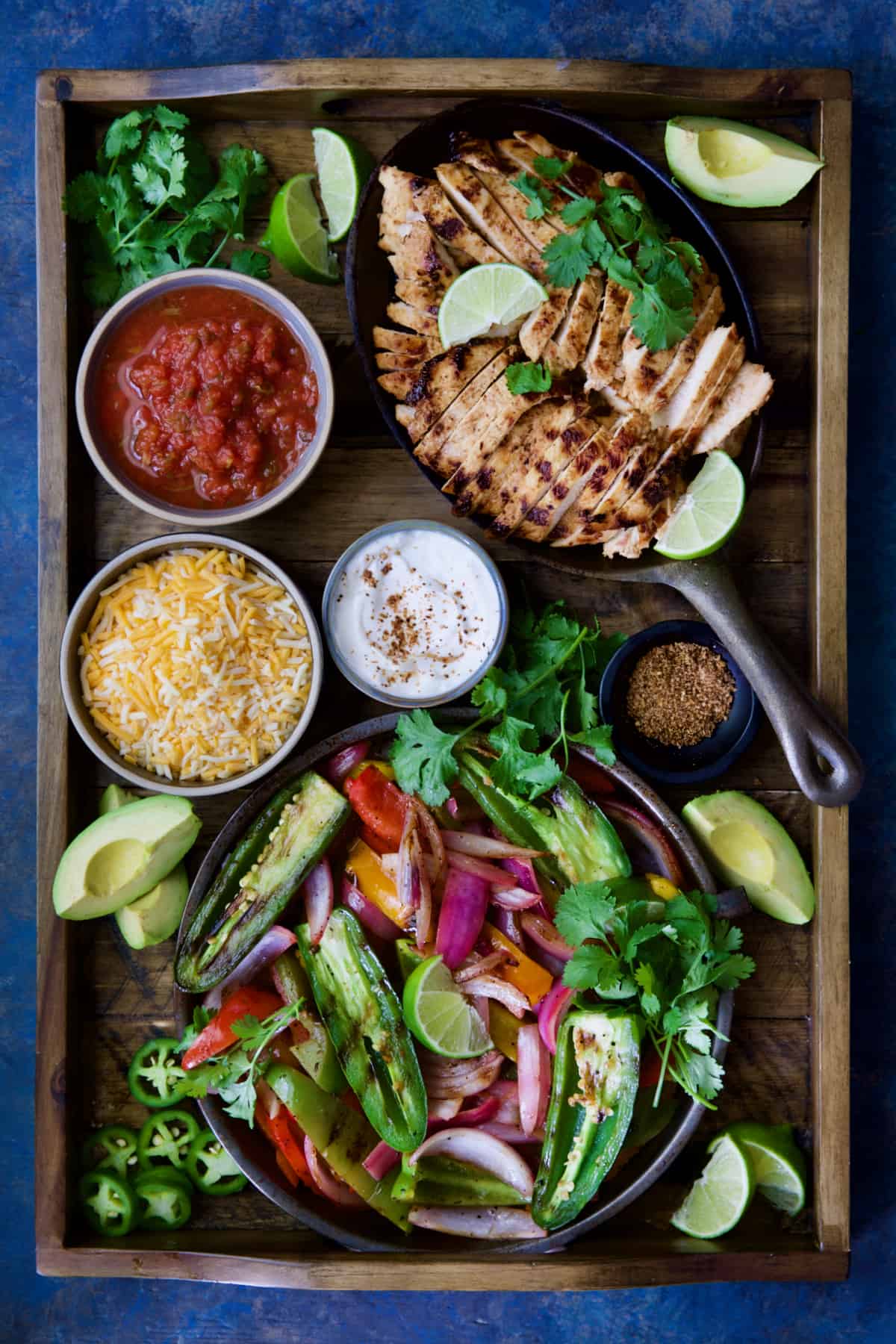 Grilled Tajin-Seasoned Chicken Fajitas on wood tray with accompaniments: Salsa, sour cream, cheese, etc.
