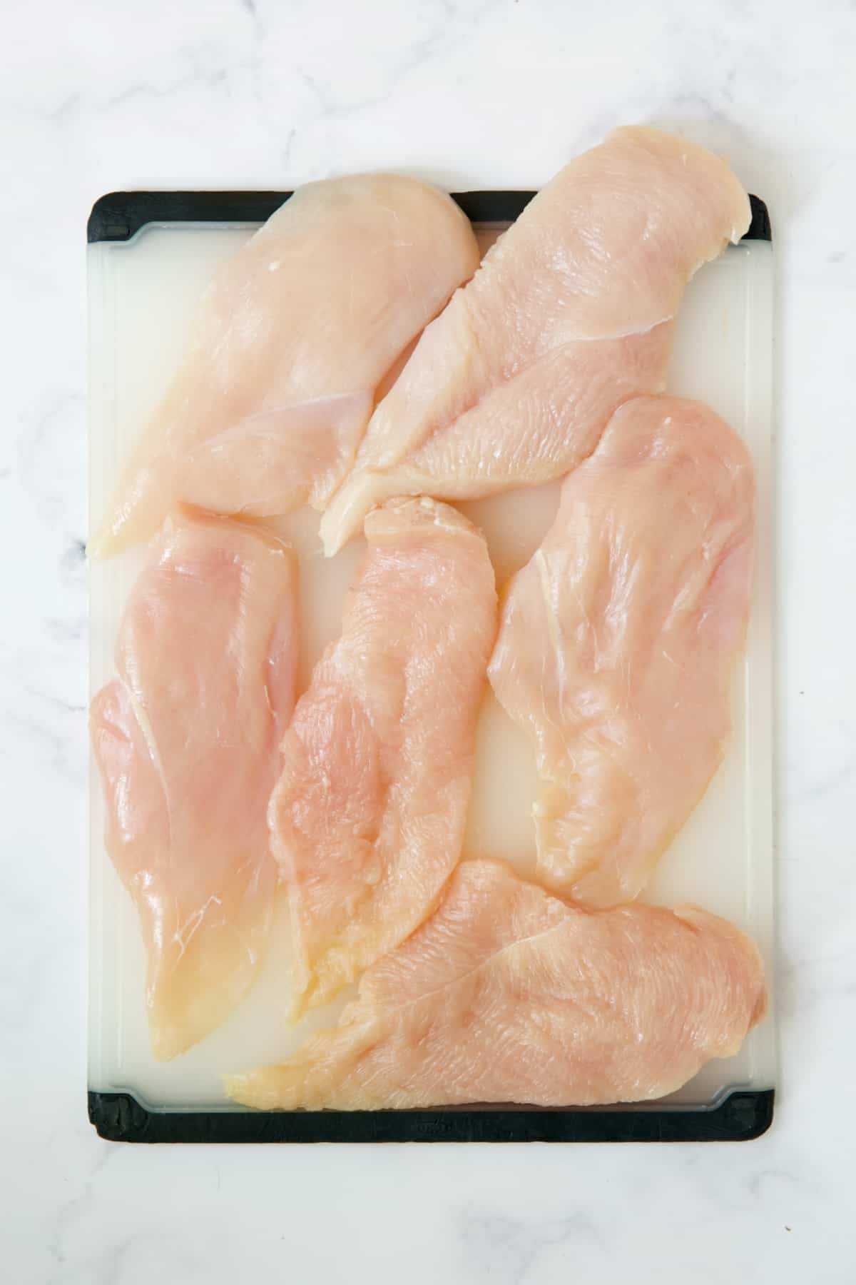 Six pieces of uncooked chicken on white cutting board.