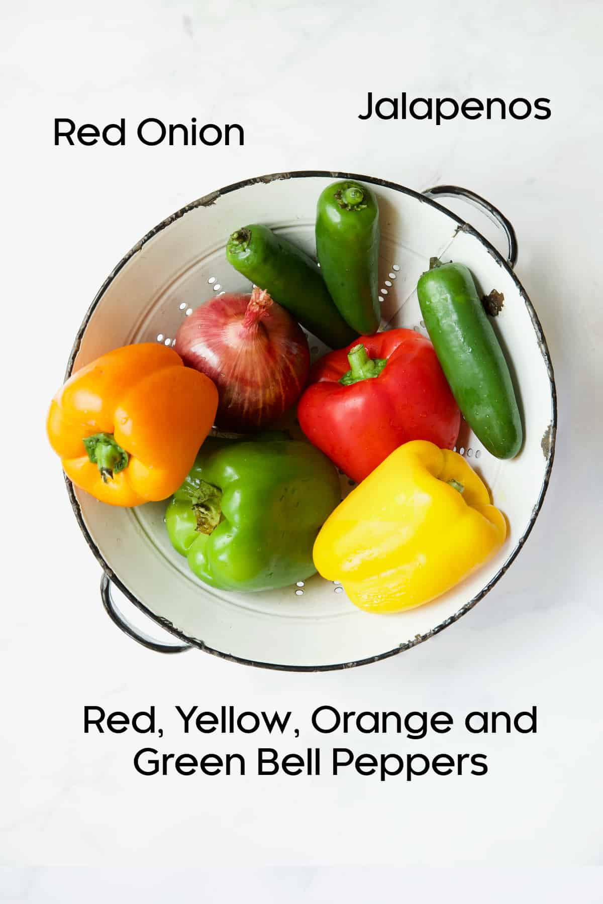 Bell peppers, onion and jalapenos in white antique colander.