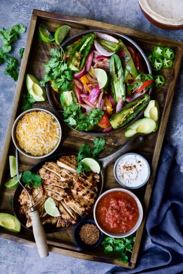 Grilled Tajin-Seasoned Chicken Fajitas on wood board with all the accompaniments.