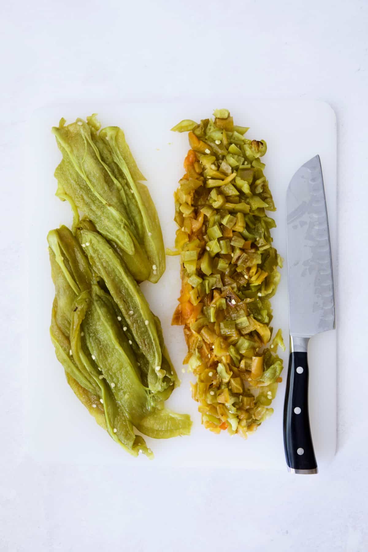 Seeded and roasted Hatch green chiles with half diced on white cutting board.