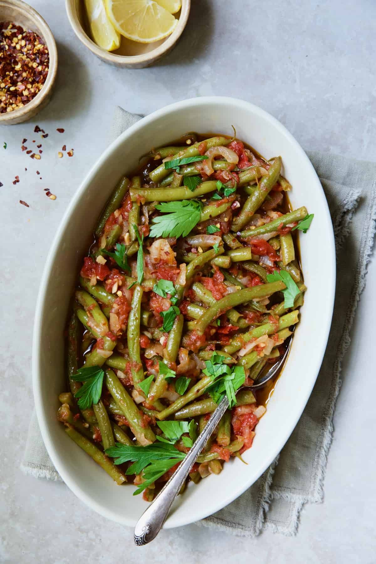 Mediterranean Braised Green Beans with Tomatoes in oval serving dish garnished with fresh parsley.
