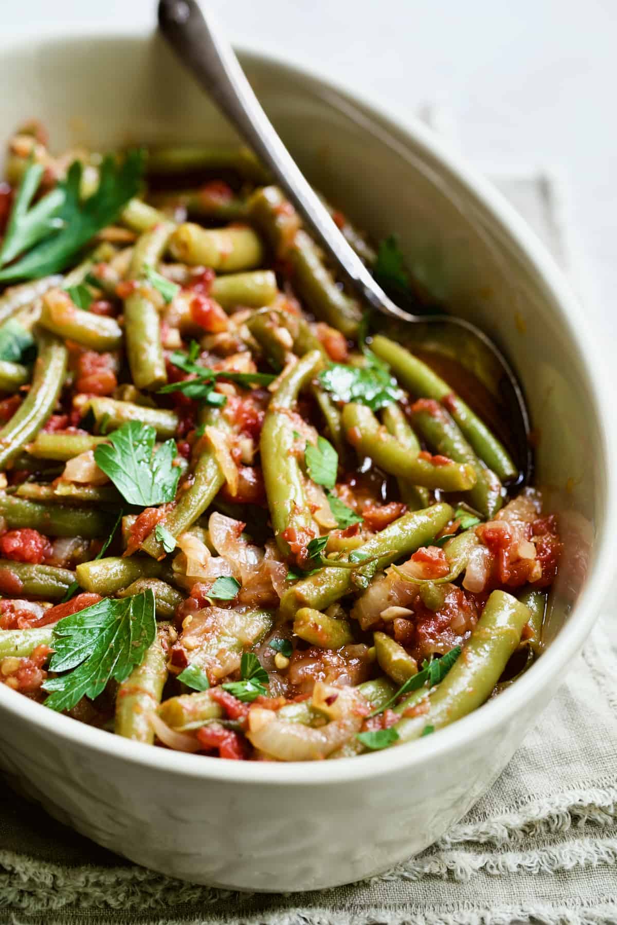 Mediterranean Braised Green Beans with Tomatoes in oval serving dish with serving spoon.