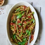 Mediterranean Braised Green Beans with Tomatoes in oval serving dish with serving spoon garnished with fresh parsley.