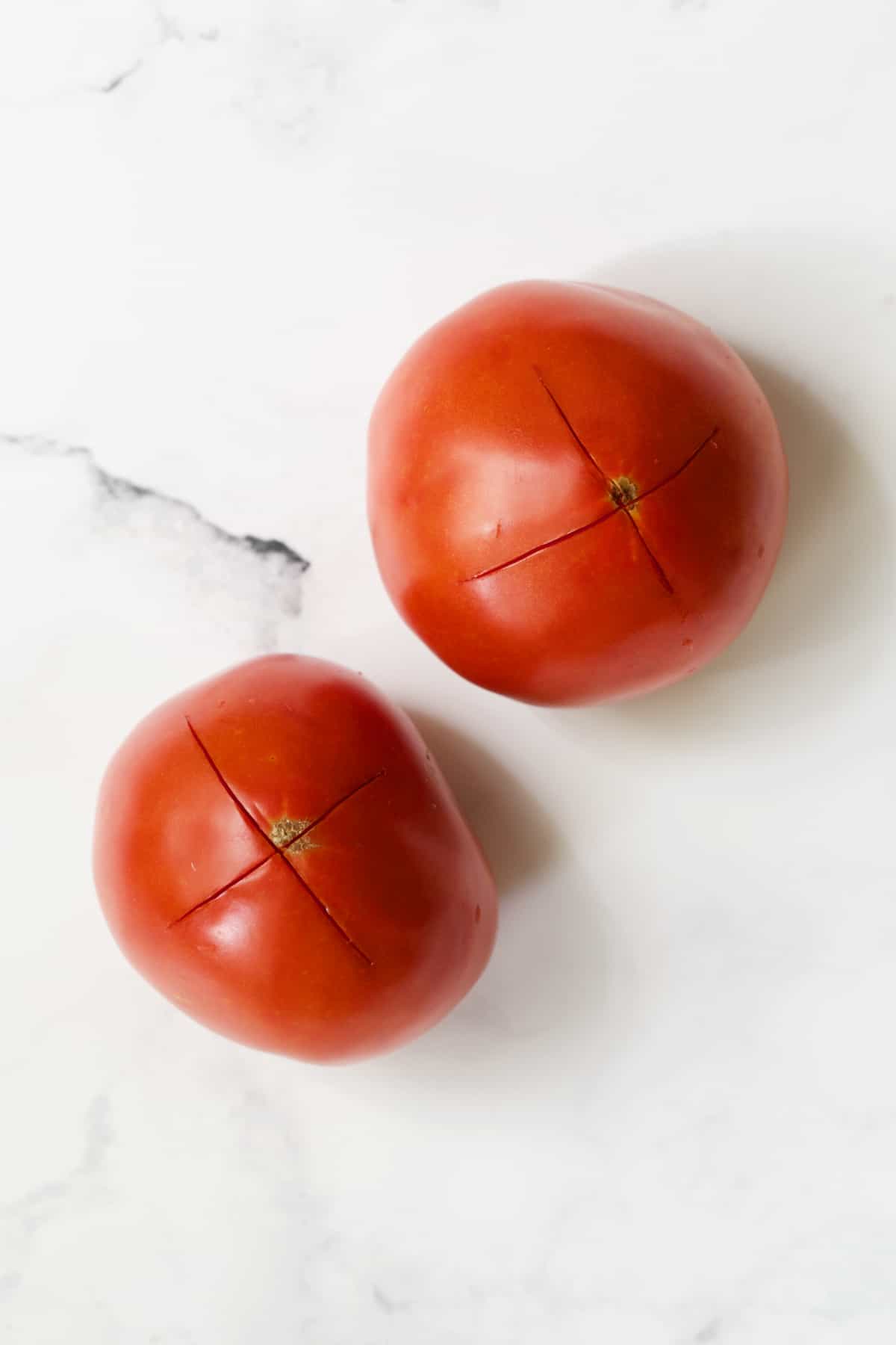 Two tomatoes on white background that have an X scored in the bottom.