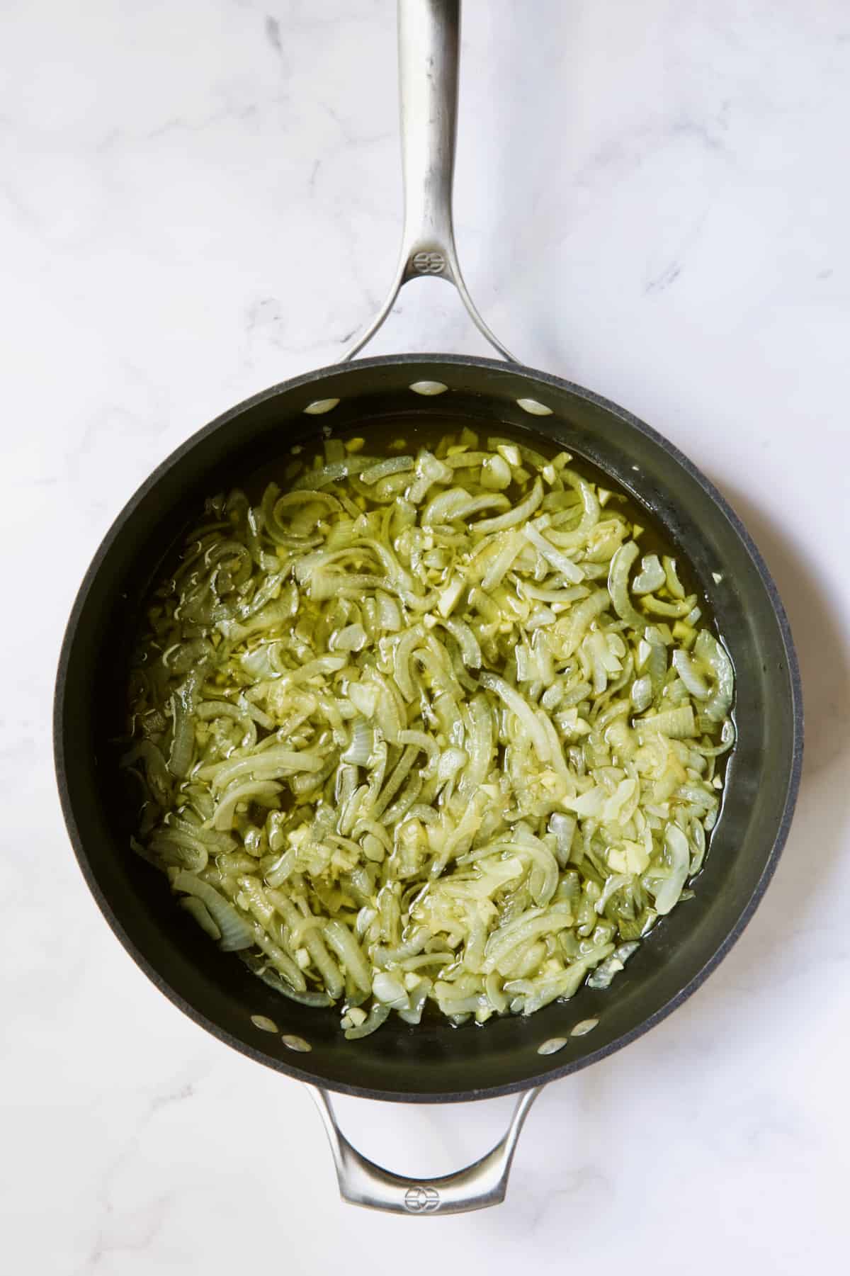 Onions being cooked in olive oil in skillet.