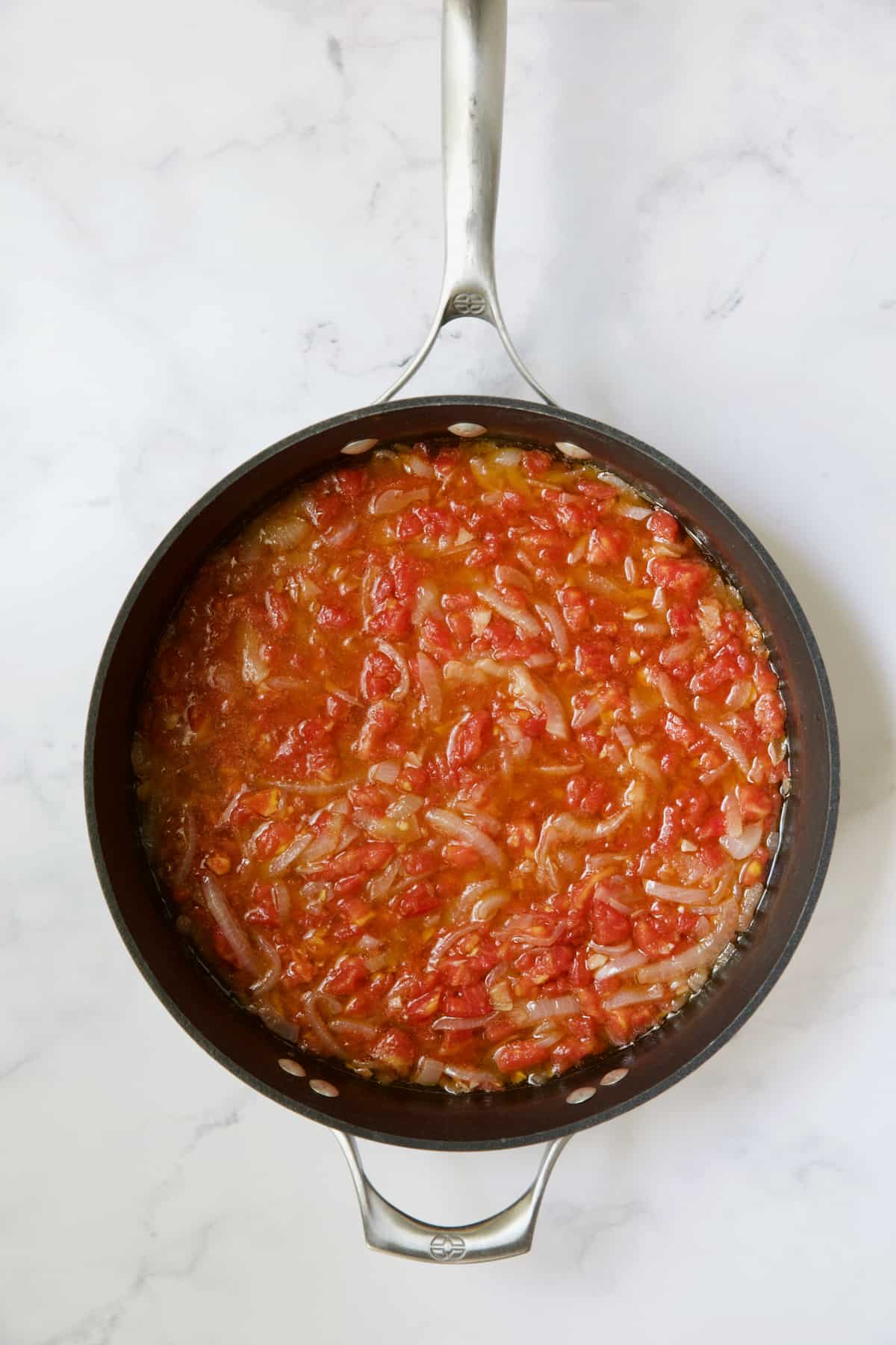 Tomatoes and onions being cooked in skillet.