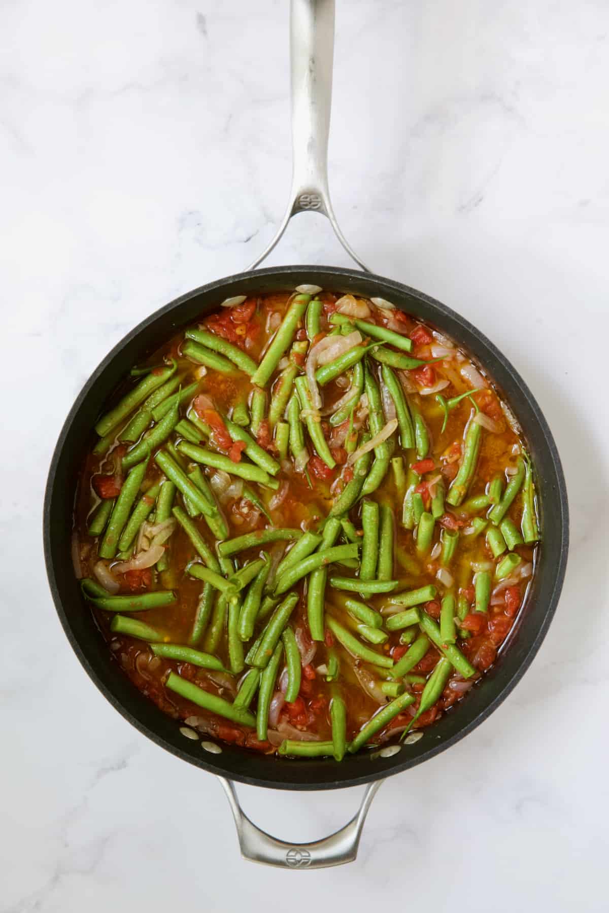 Green beans and tomatoes cooking in skillet right after fresh green beans are added.