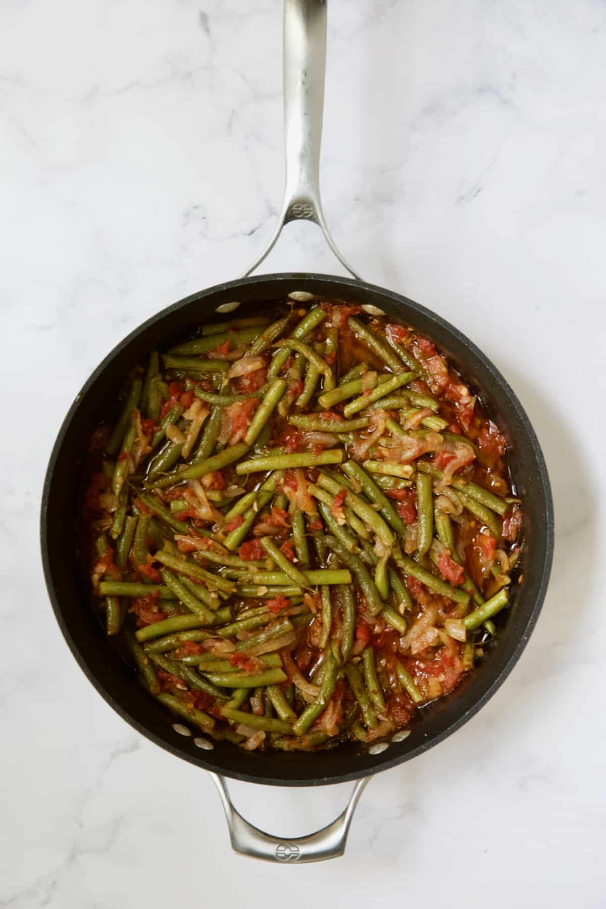 Cooked green beans and tomatoes in skillet.