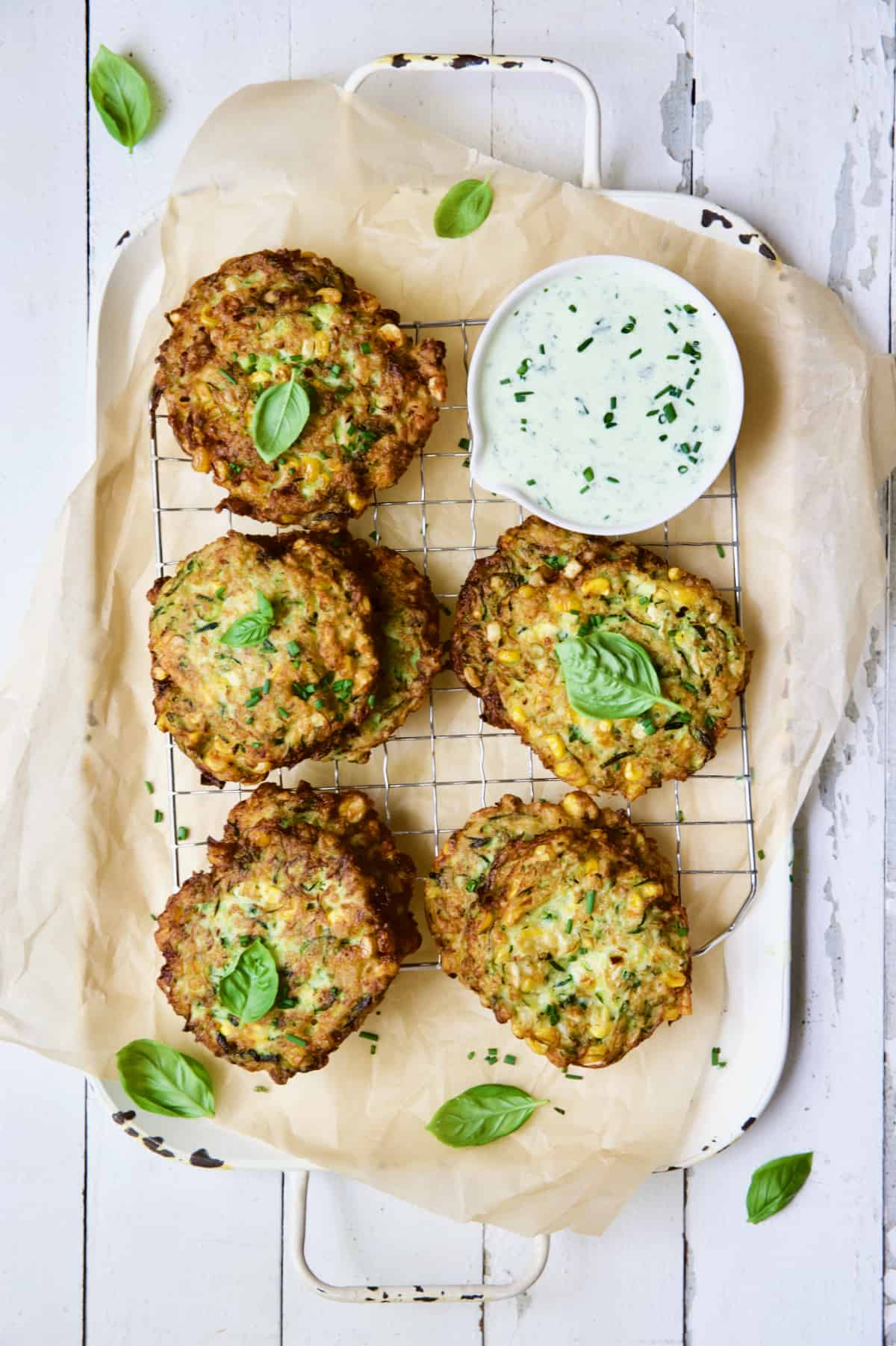 Zucchini Corn Fritters with Basil Buttermilk Sauce on parchment paper lined tray on white background.