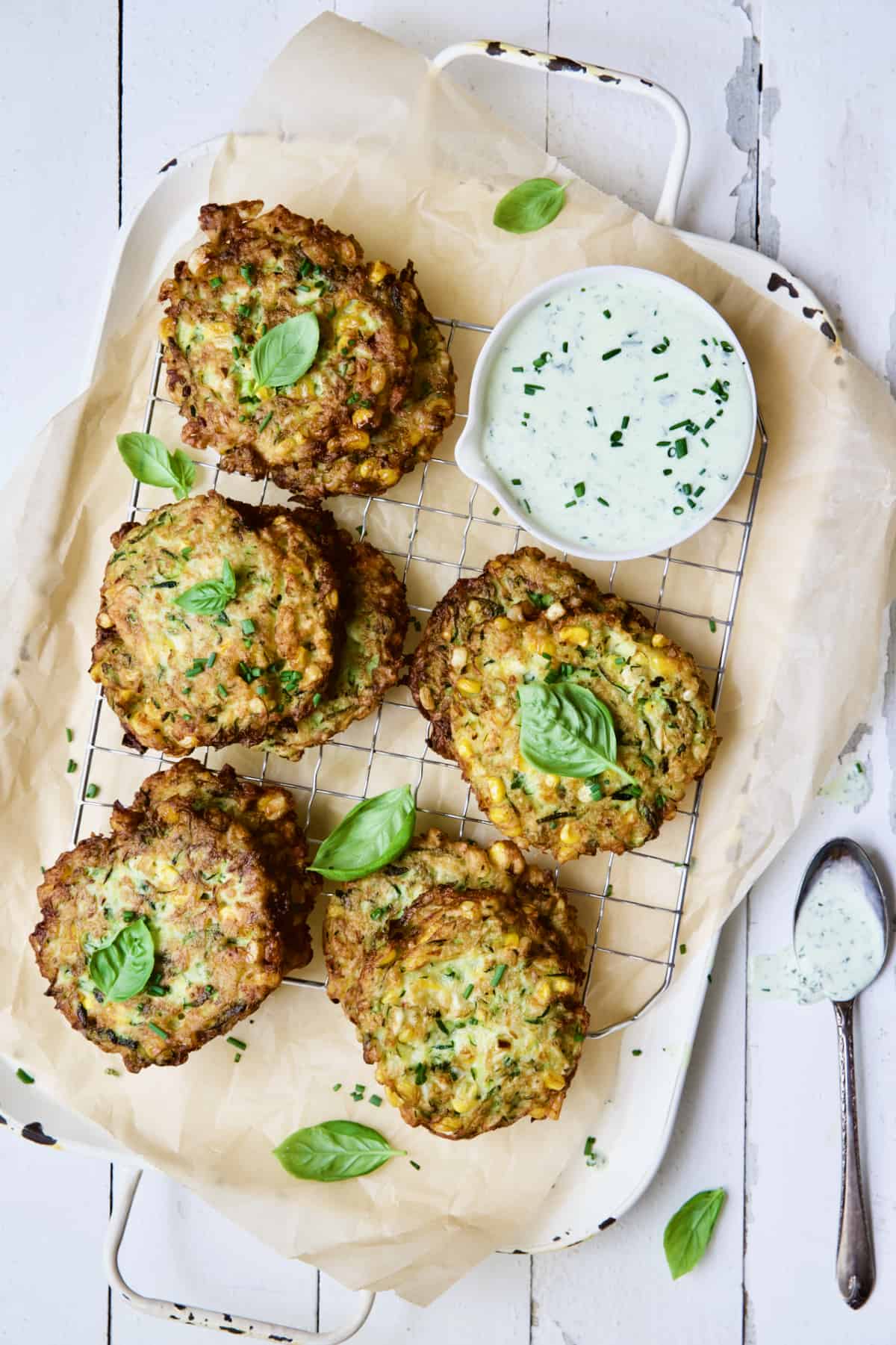 Zucchini Corn Fritters with Basil Buttermilk Sauce on white background garnished with fresh basil.