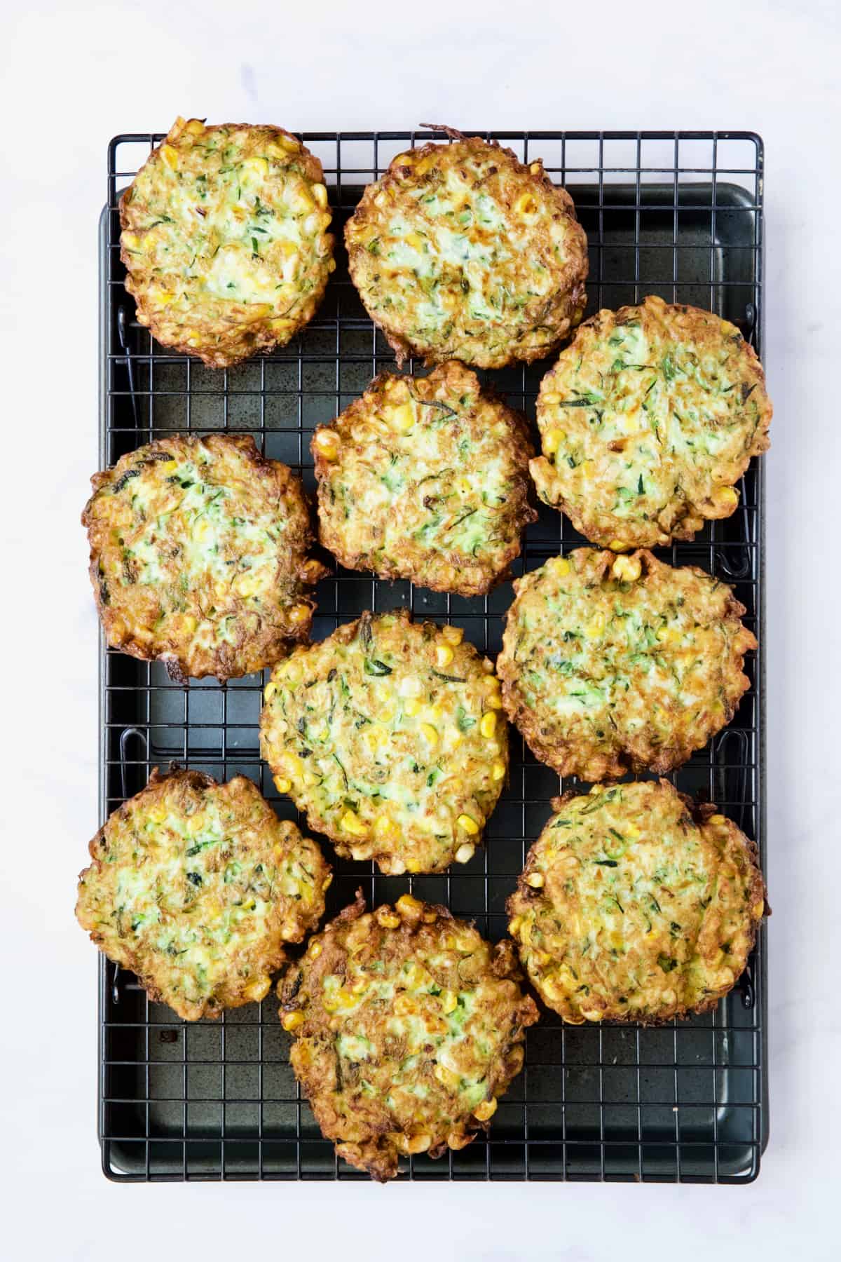 Ten Zucchini Corn Fritters on rack set over baking sheet.