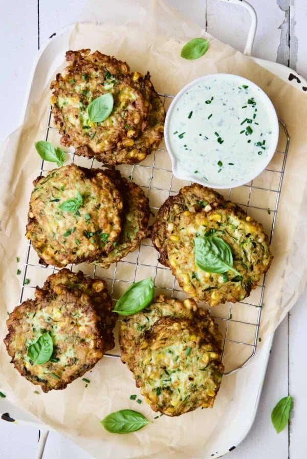 Zucchini Corn Cakes with Basil Buttermilk Sauce on cooling rack garnished with fresh basil.