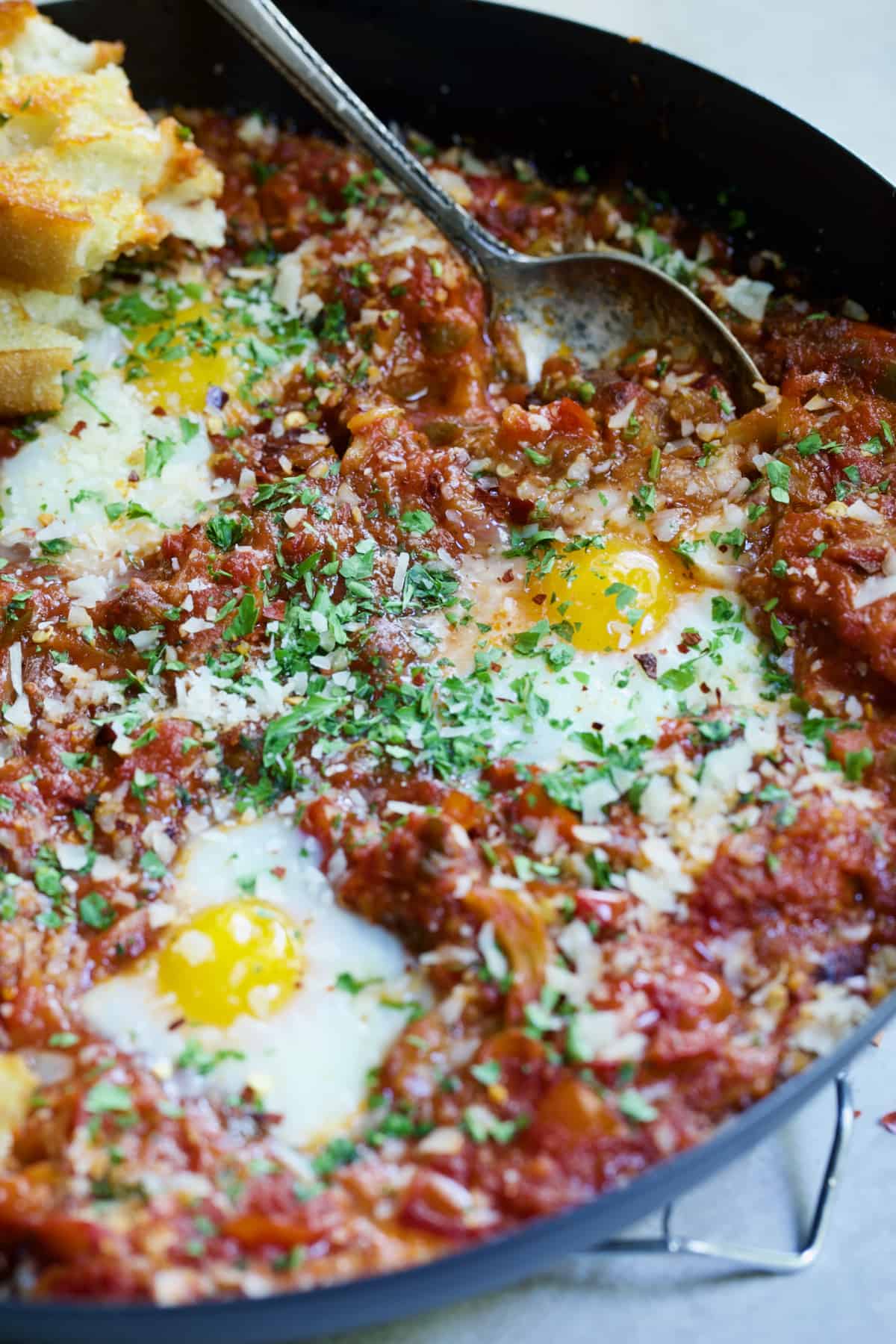 Eggs in Purgatory with Italian Sausage with serving spoon in black skillet.