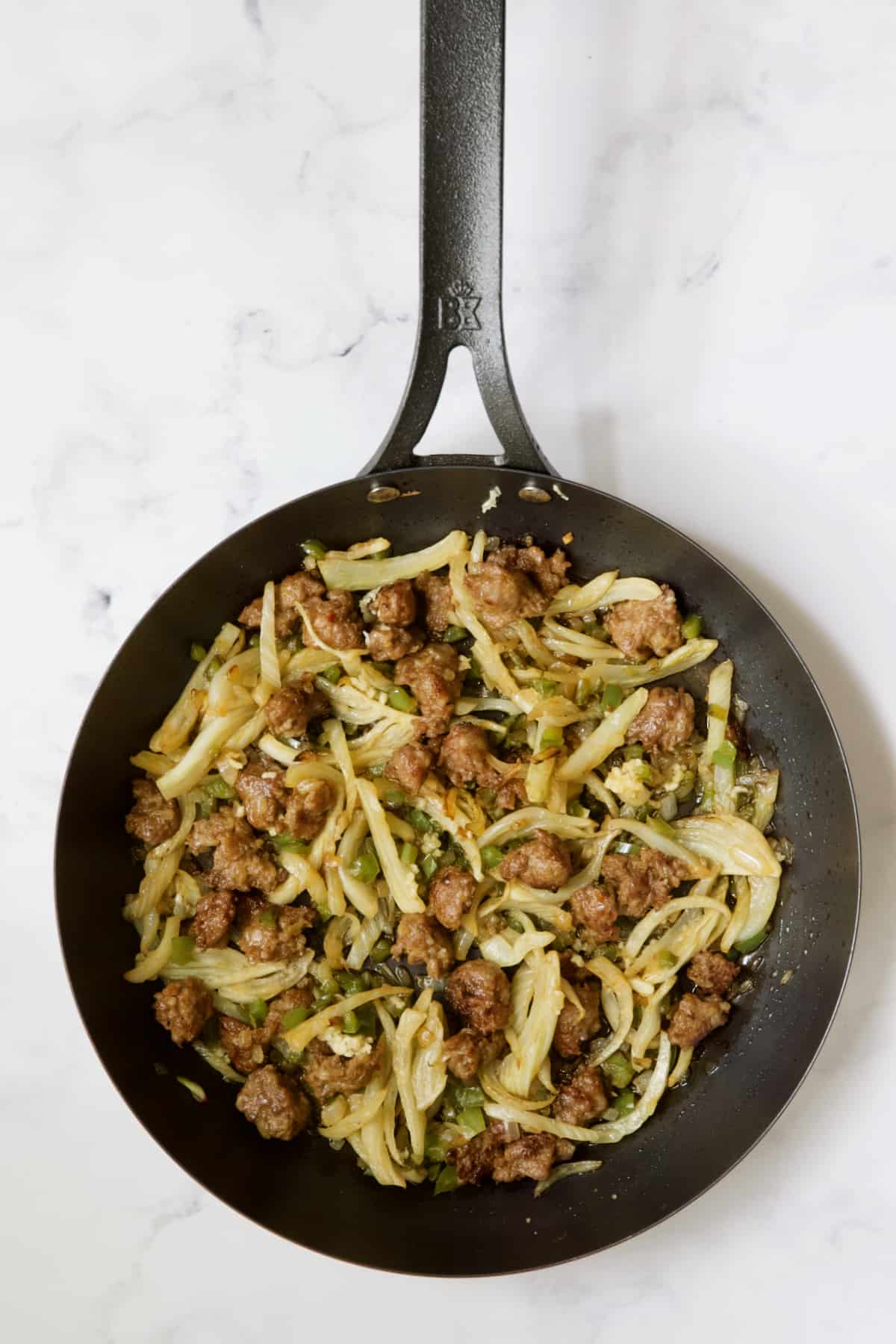 Cooked Italian sausage, fennel, onions and green pepper in black skillet.