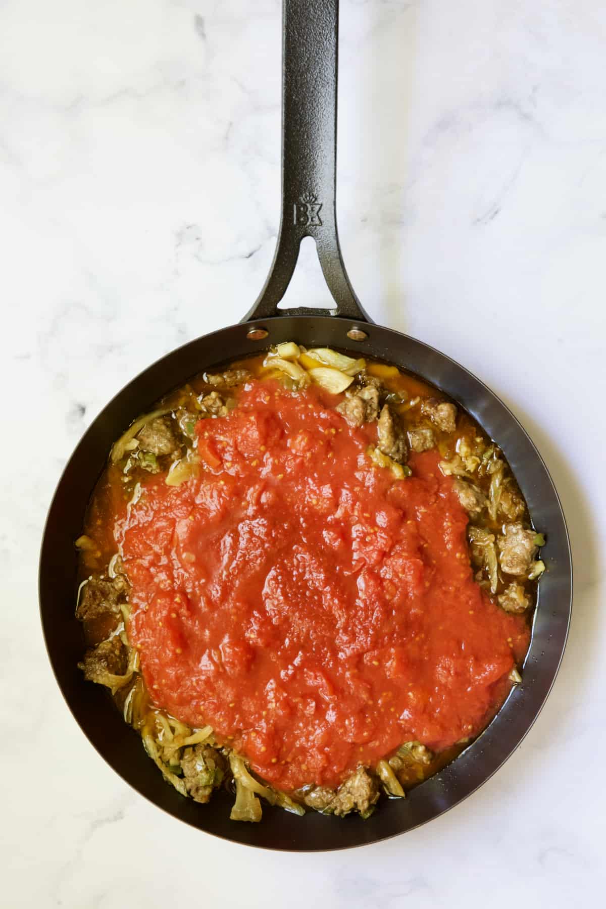 Sauce added to cooked Italian sausage and vegetables in black skillet.