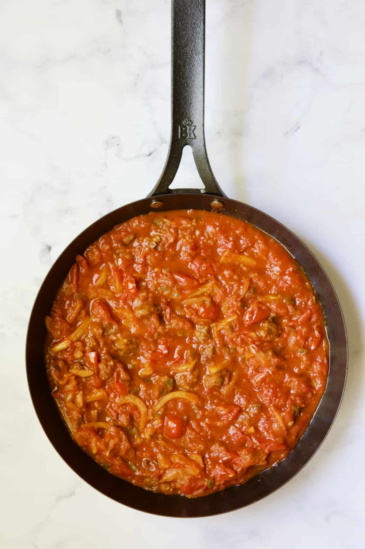 Tomato sauce with sausage in black skillet.