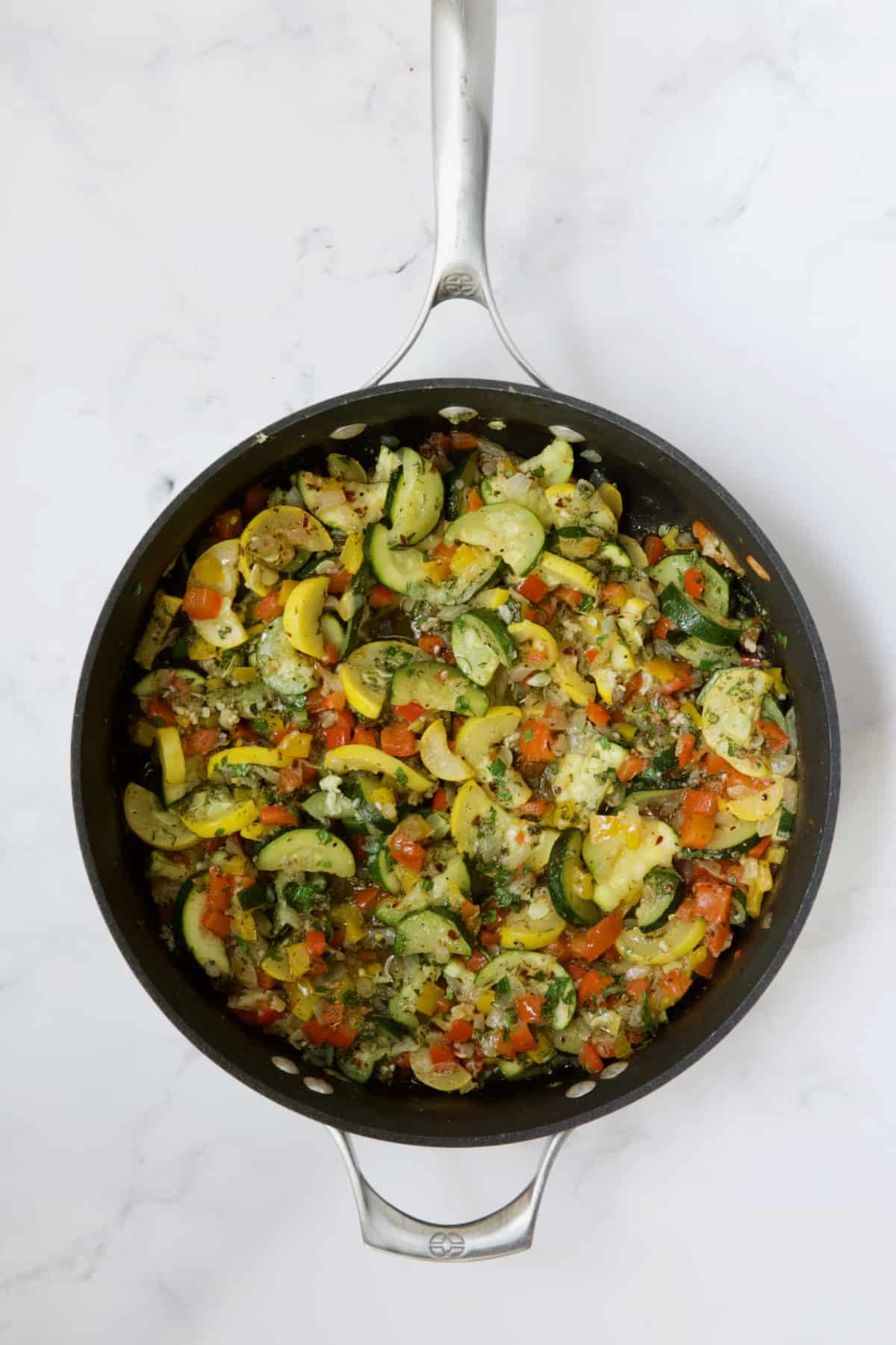 Cooked onions, peppers, zucchini and yellow squash in skillet.