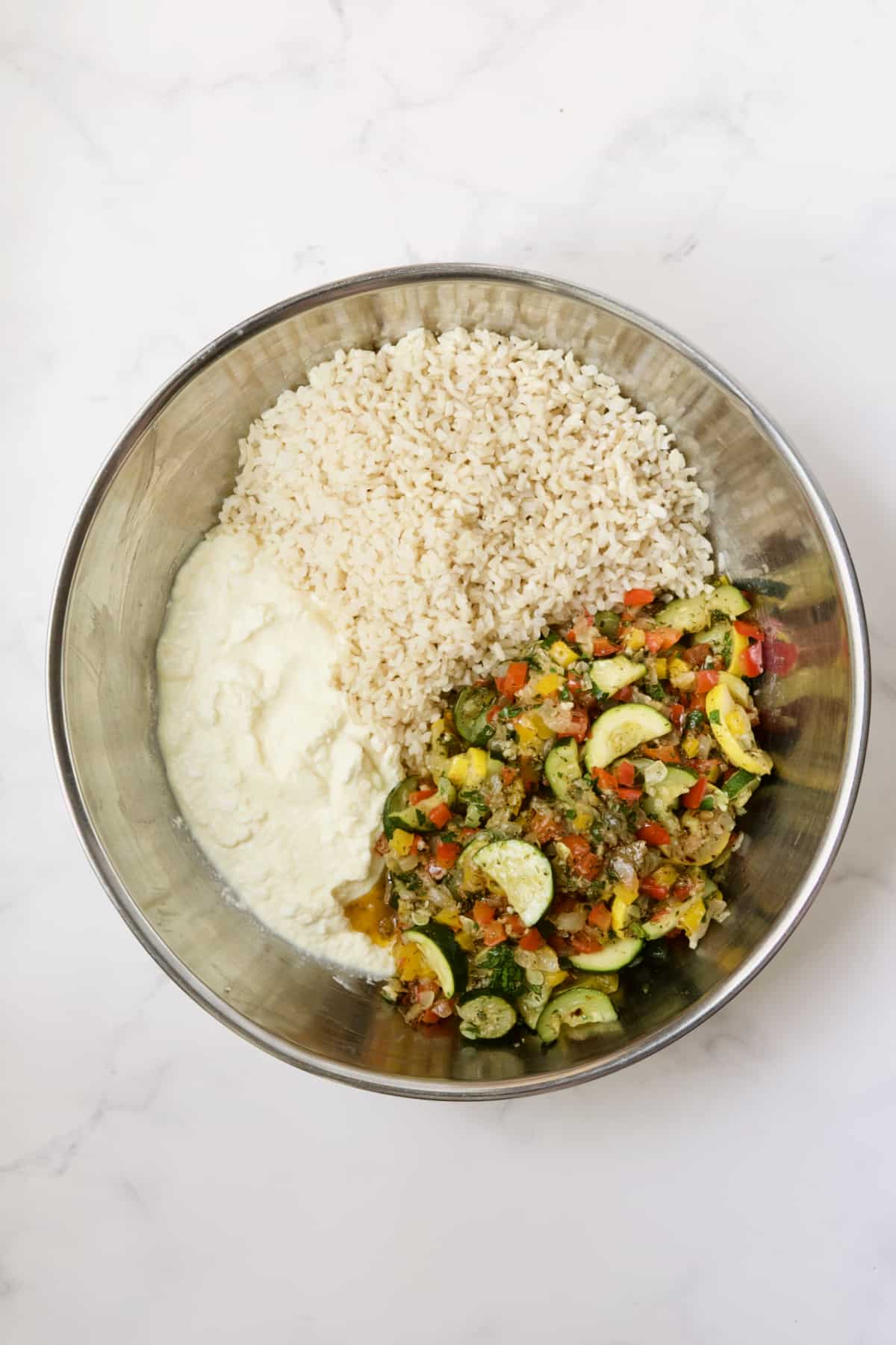 Ingredients for Greek Brown Rice and Vegetable Casserole in stainless steel bowl before being stirred together.