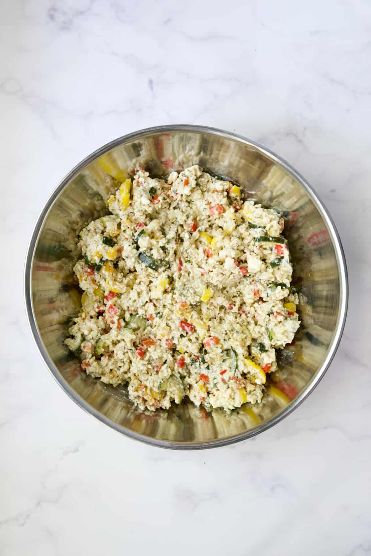 Ingredients for Greek Brown Rice and Vegetable Casserole stirred together in stainless steel bowl.
