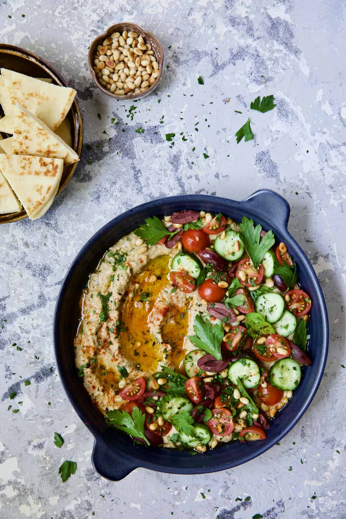Loaded Roasted Eggplant Dip (Baba Ganoush) in blue dish on distressed background with pita chips and pine nuts.