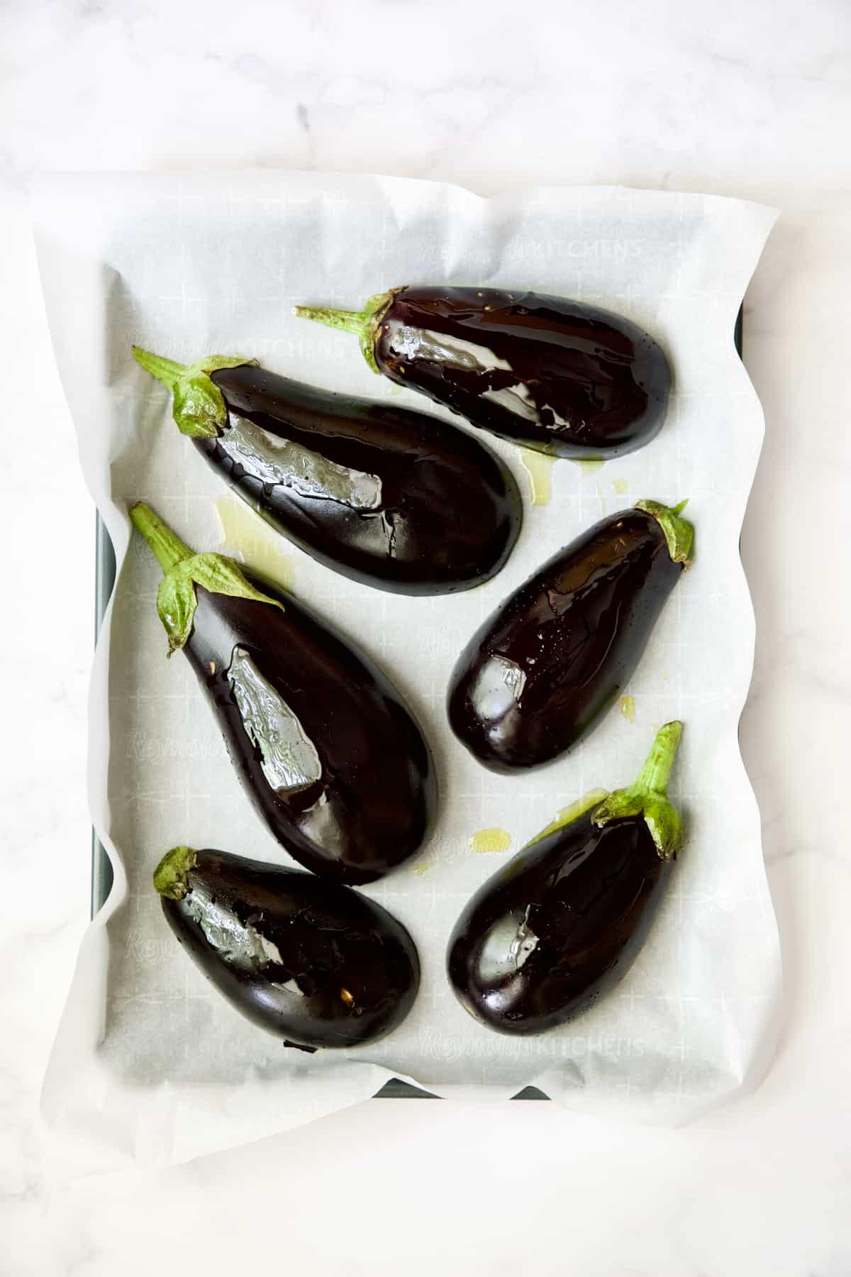 Six eggplant halves on parchment paper-lined baking sheet before being roasted.