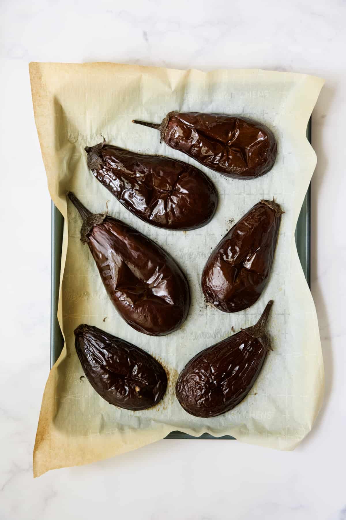 Six roasted eggplant halves on parchment paper-lined baking sheet.