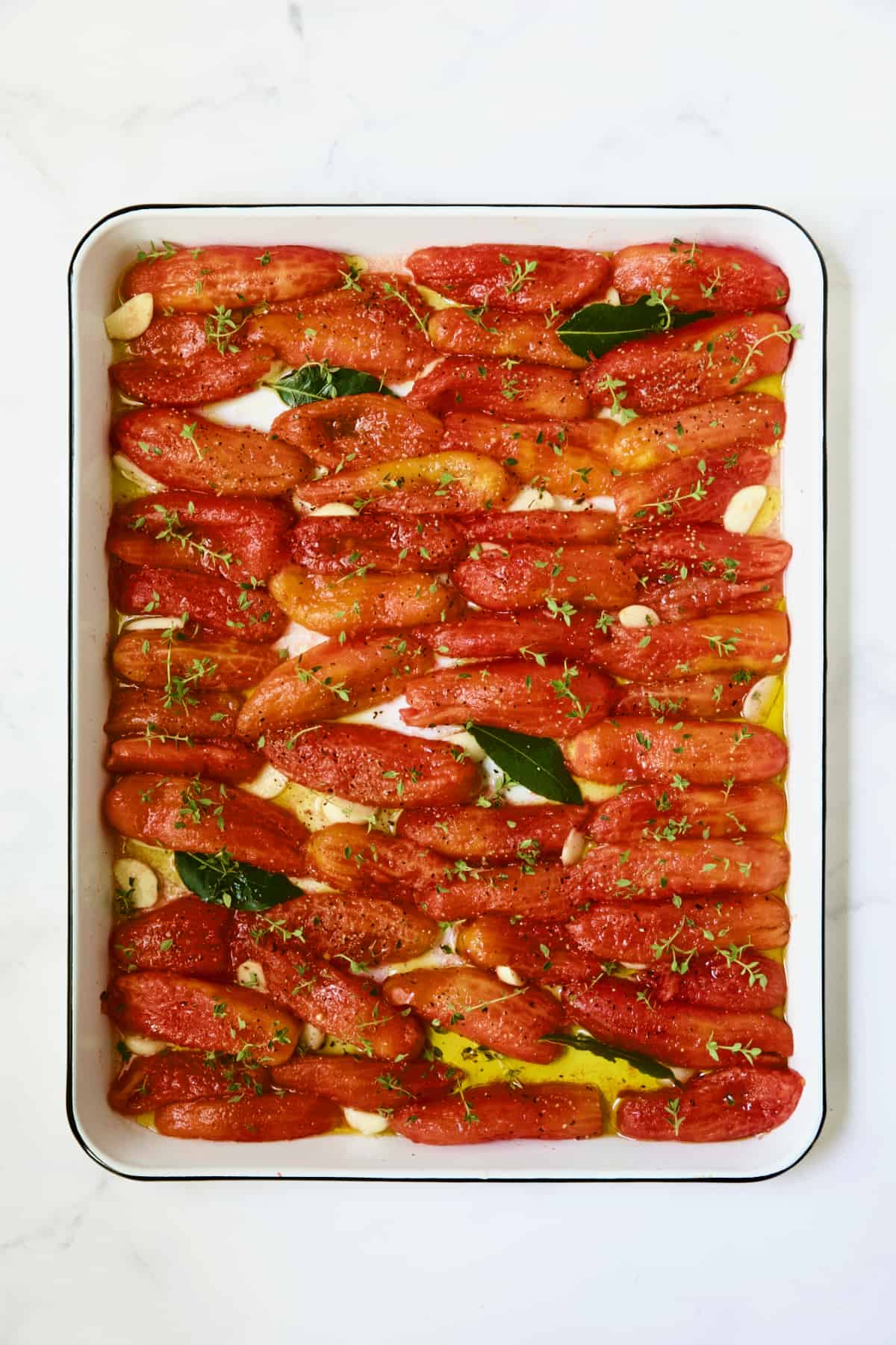 Tomatoes on white enameled baking sheet before being slow-roasted.