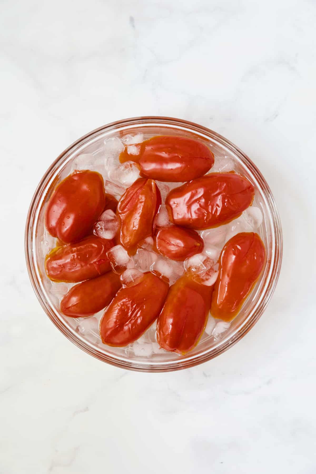 Roma tomatoes after being blanched in ice water in glass bowl.