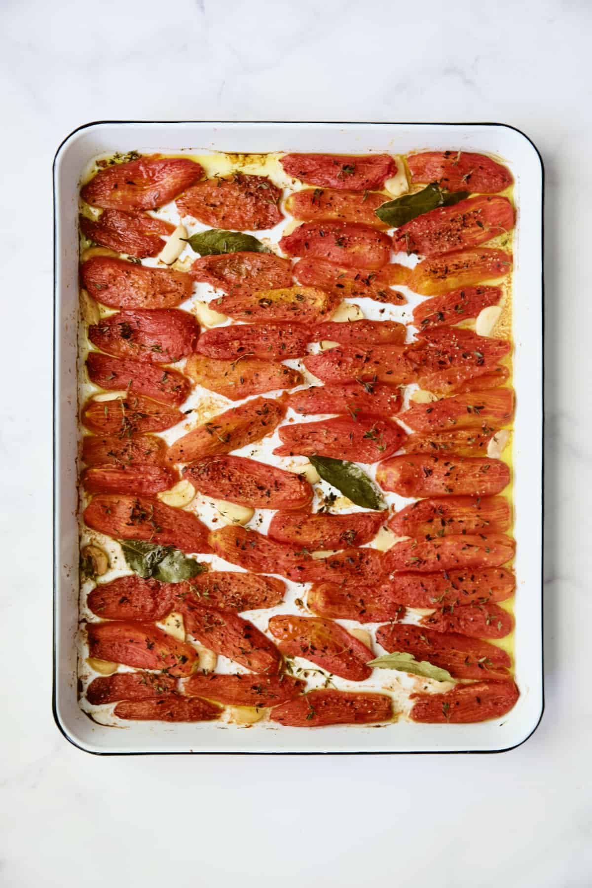 Confit tomatoes on white enameled baking sheet.