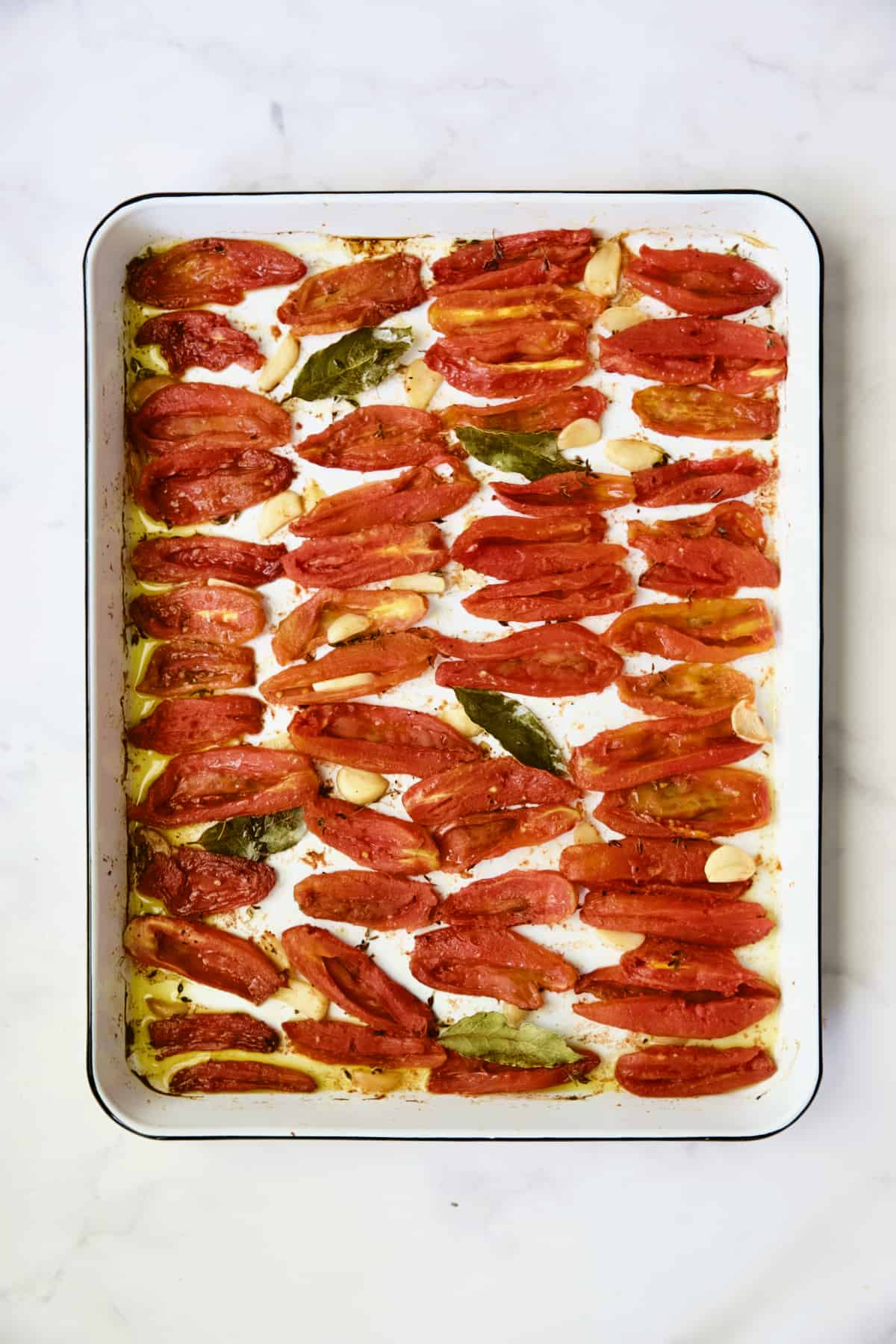 Confit tomatoes on white enameled baking sheet.