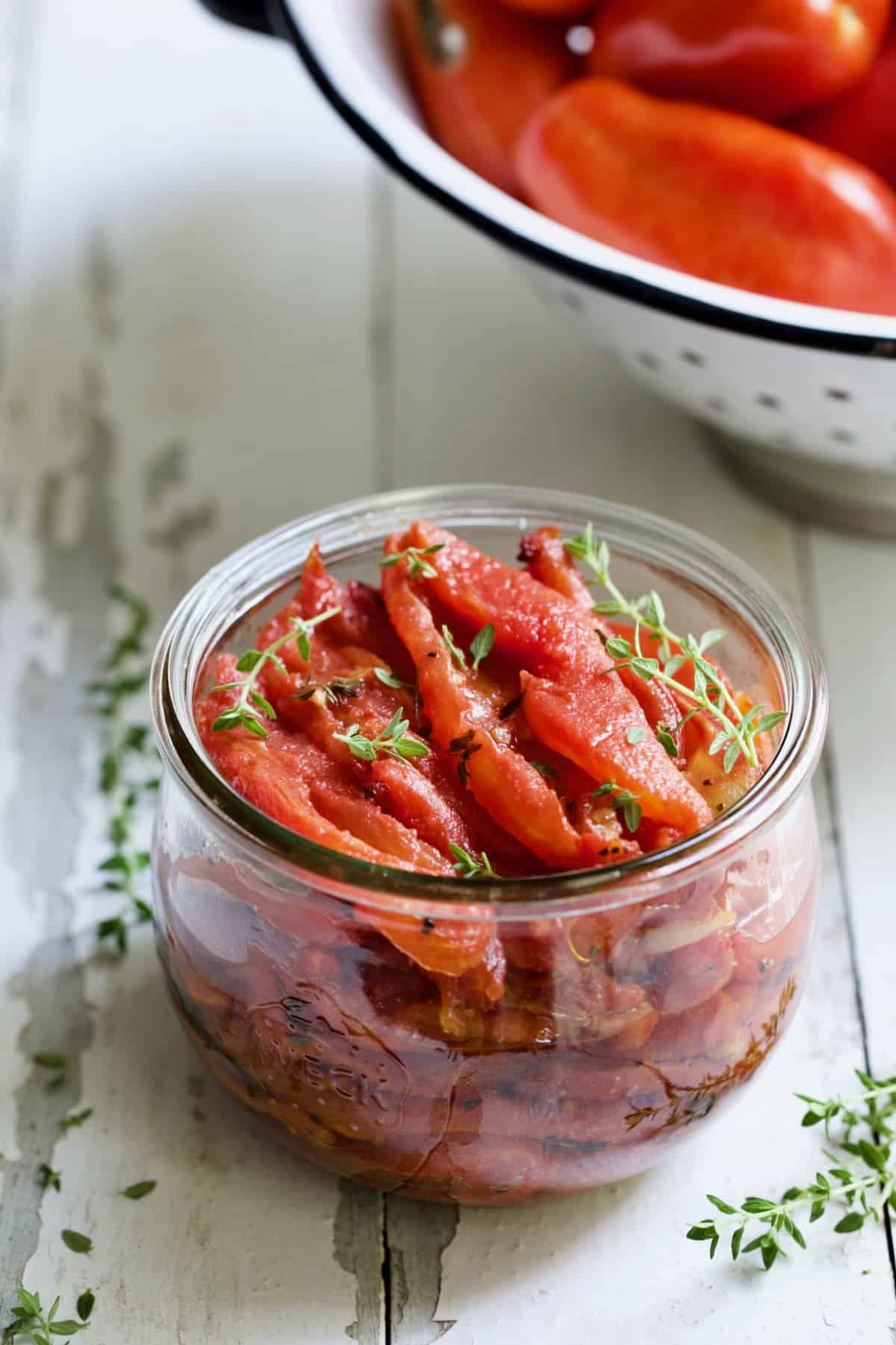 Tomato Confit in glass jar garnished with fresh thyme.