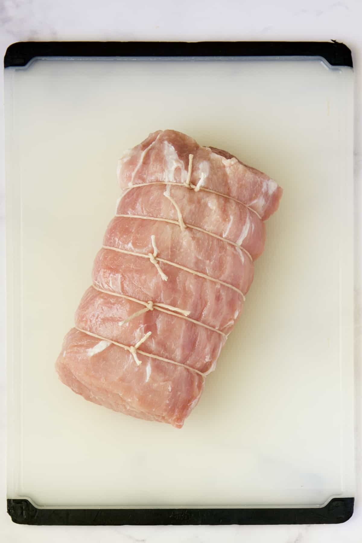 Pork loin roast on white plastic cutting board.