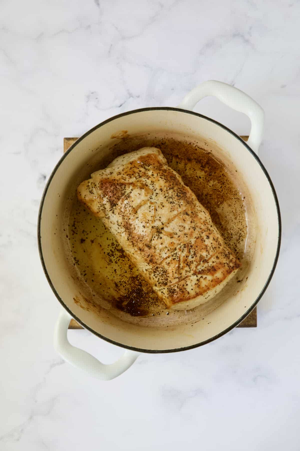Browned pork loin in white Dutch oven.
