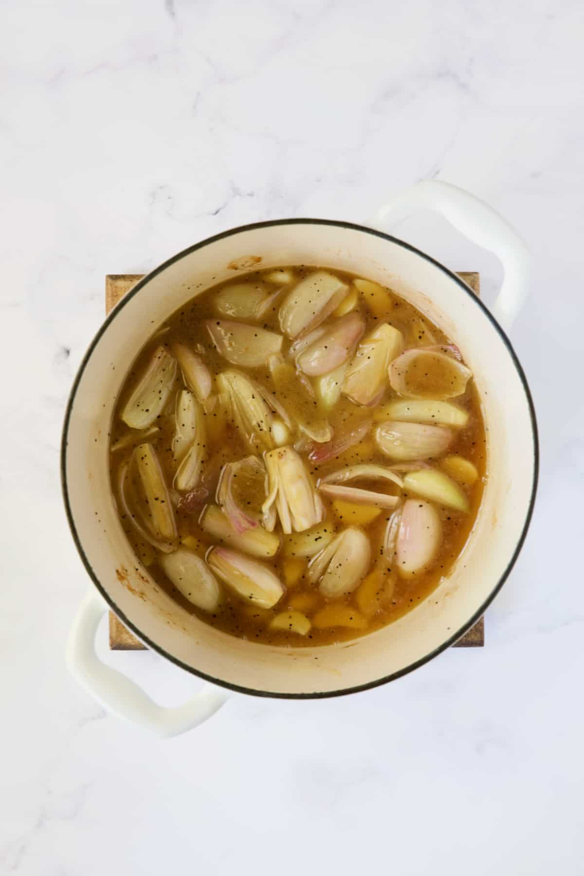 Shallots and garlic with braising liquid in white Dutch oven.