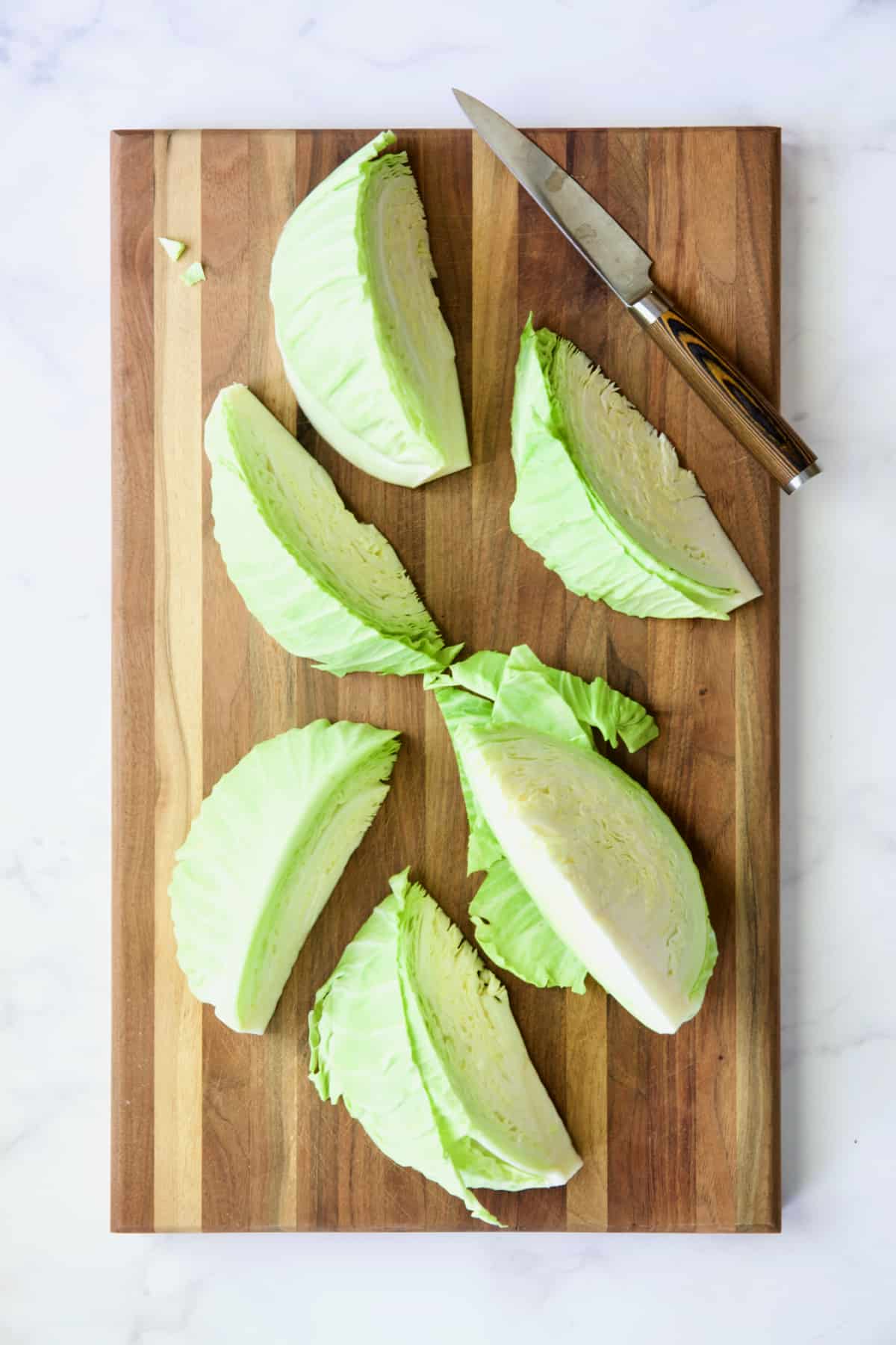 Six cabbage wedges on wood cutting board with knife.